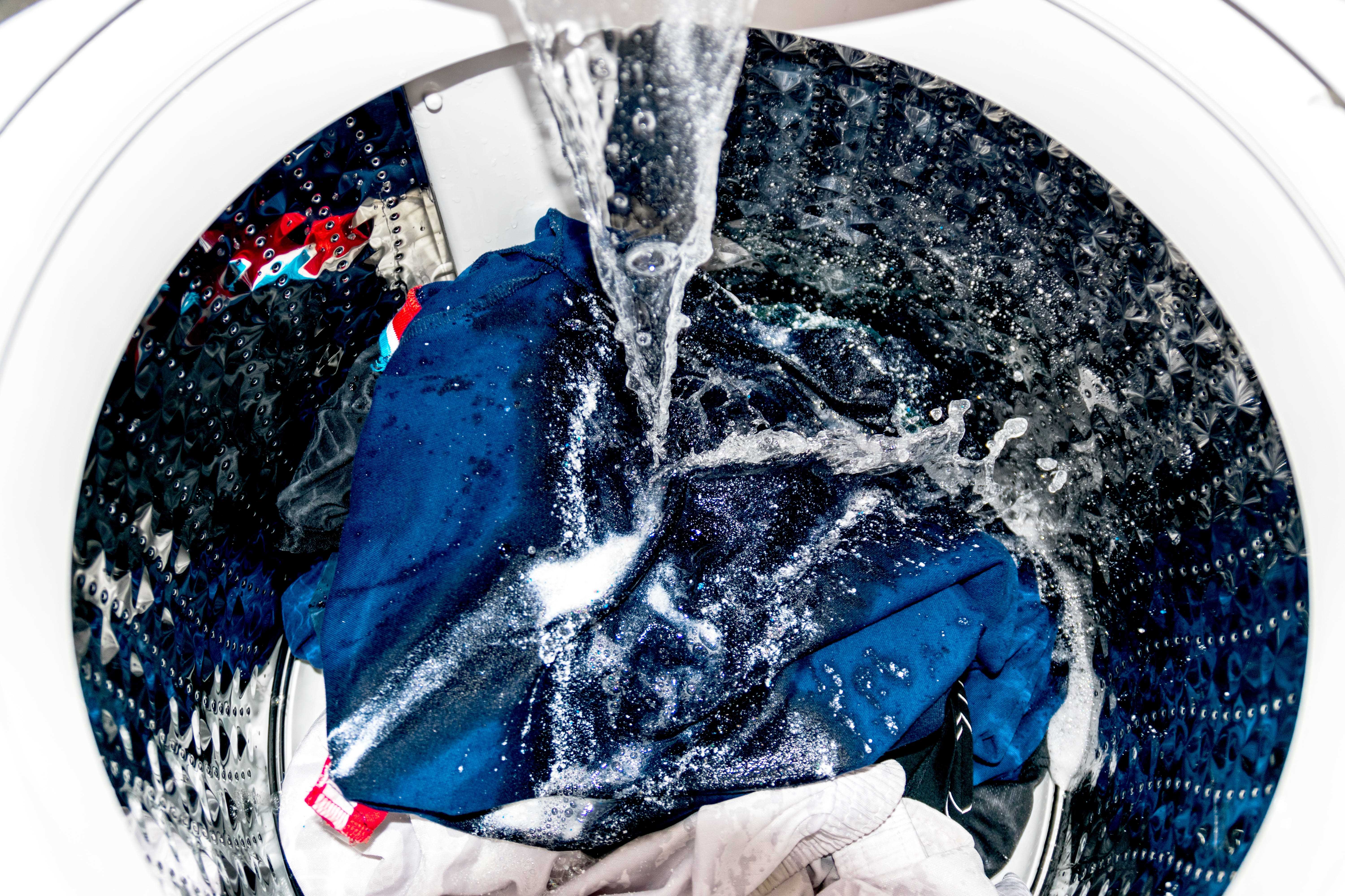 Das Innere einer Waschmaschine mit Kleidung, während sie sich mit Wasser füllt.