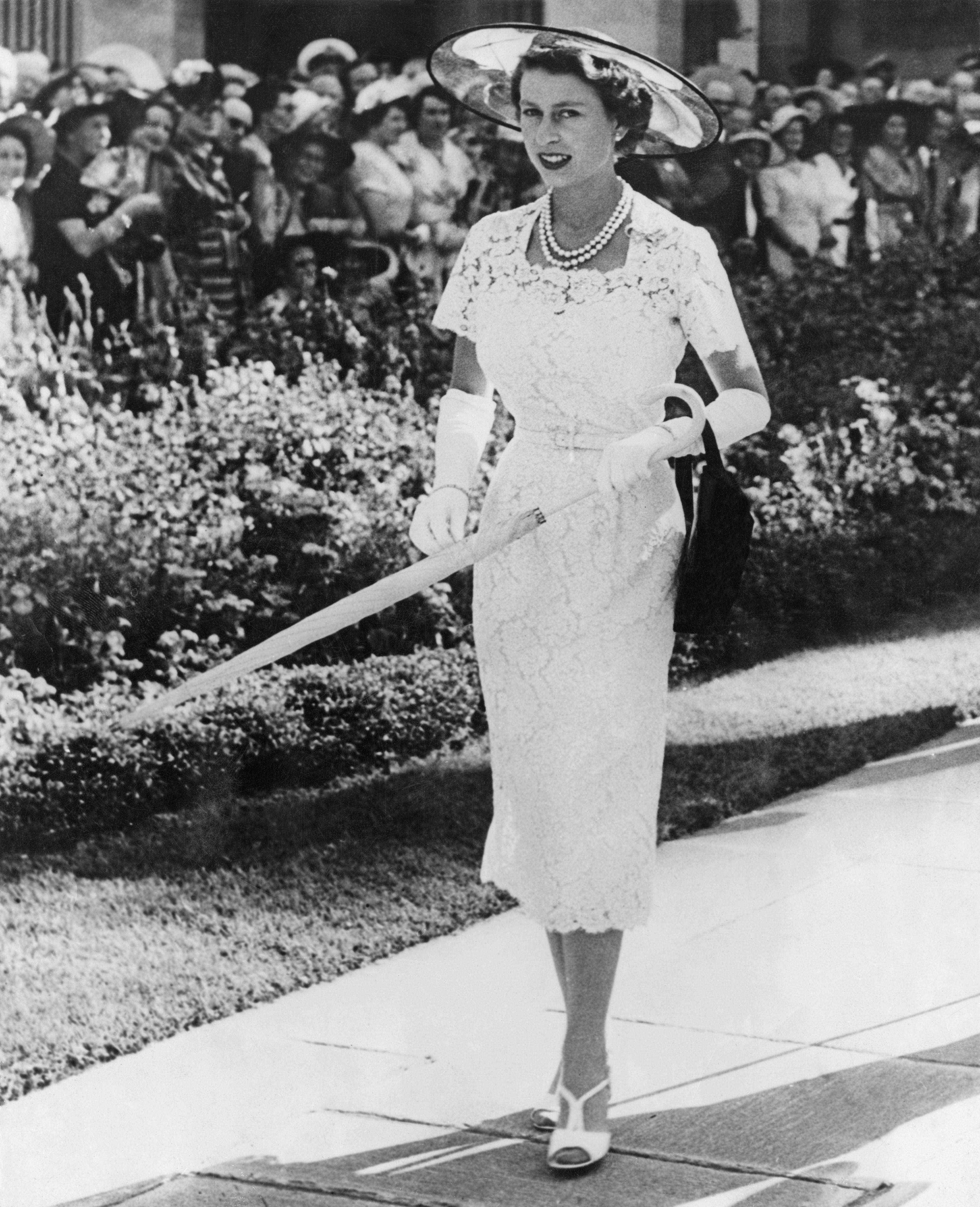 Queen Elizabeth trägt ein eng anliegendes weißes Spitzenkleid und einen Hut
