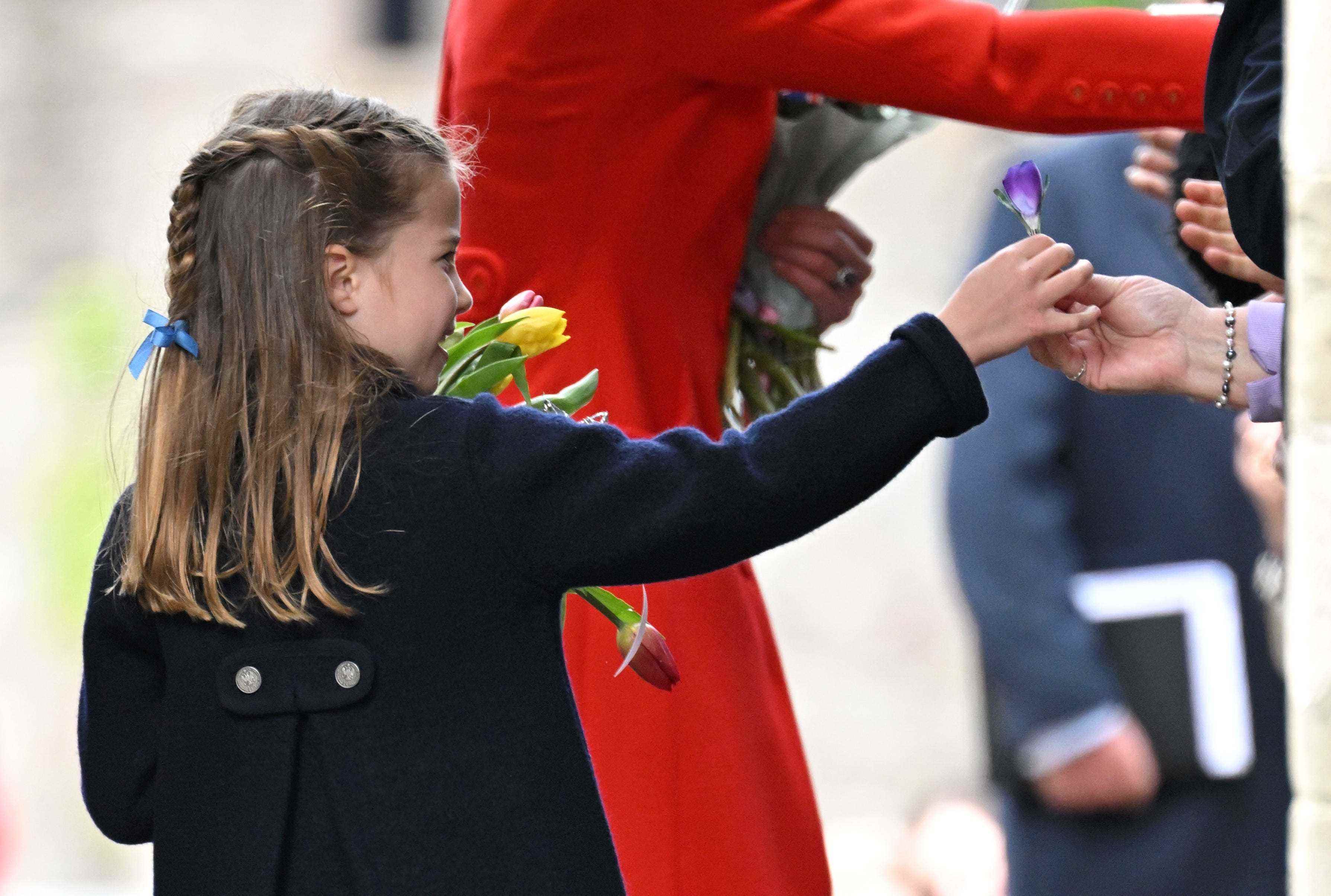 Prinzessin Charlotte überreicht jemandem außerhalb des Bildschirms eine lila Blume