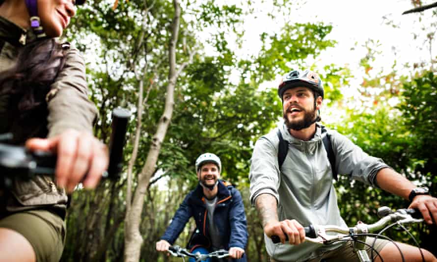 Drei Leute auf Fahrrädern lächeln und unterhalten sich in einem Wald