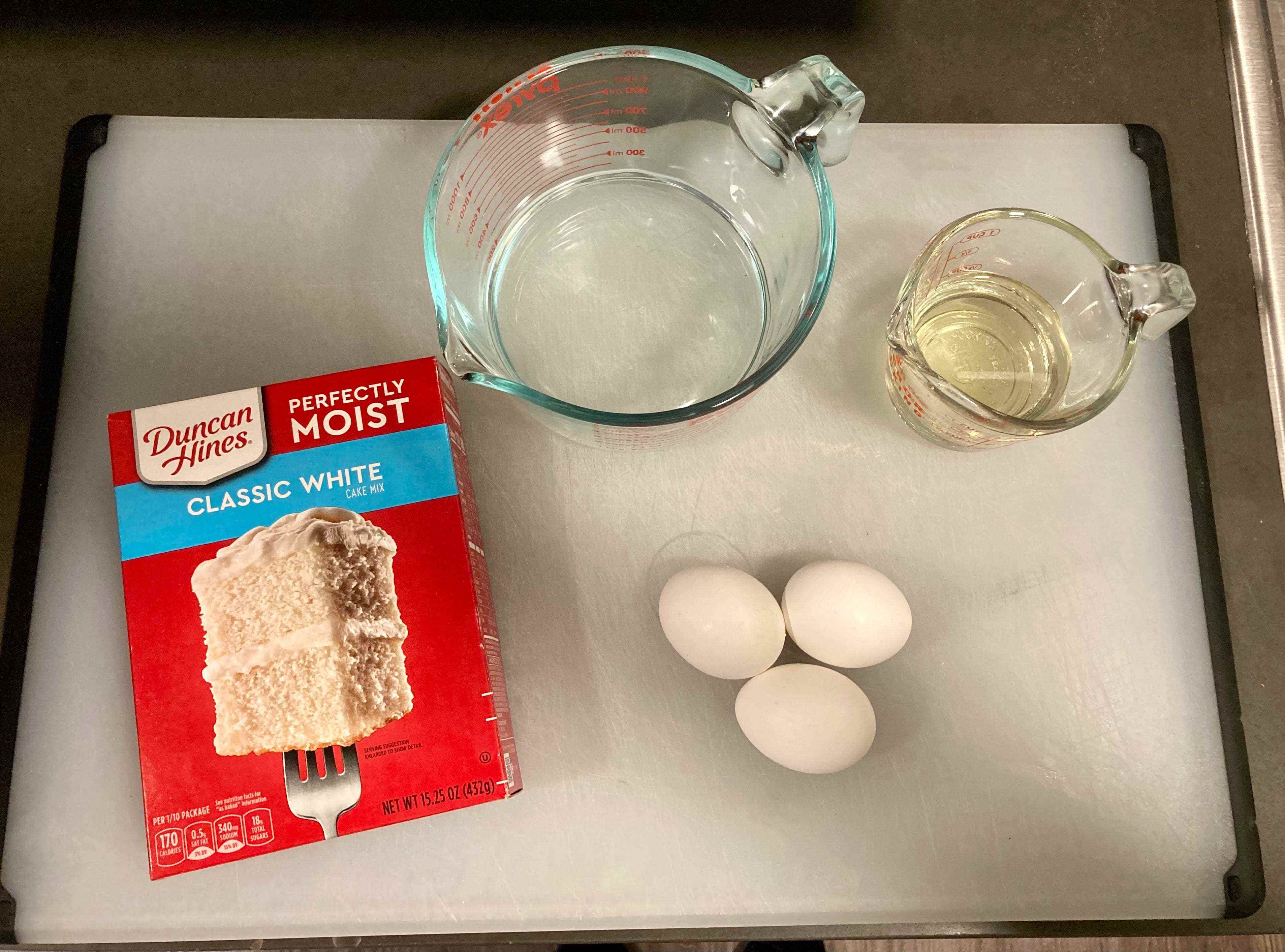 Ein Duncan Hines Vanilla Boxed Cake Mix auf einem weißen Tablett mit Messbechern mit Öl und Wasser und Eiern