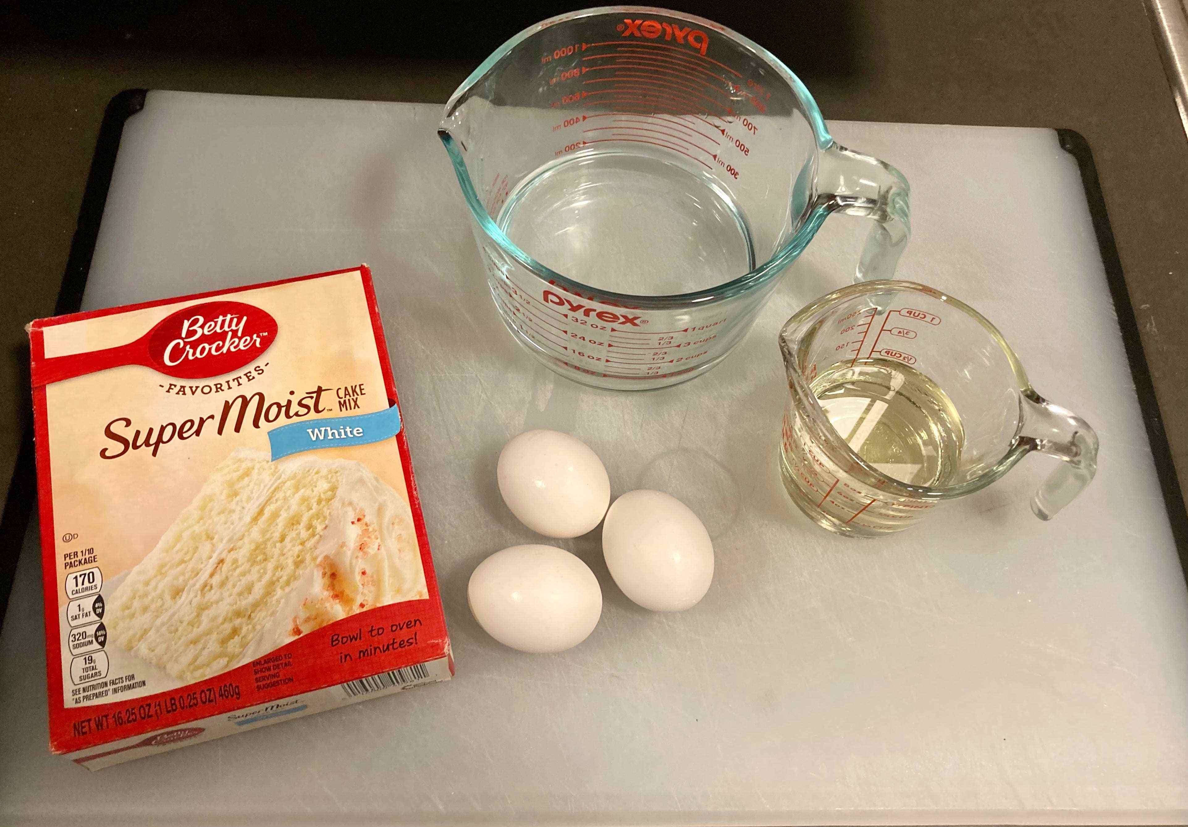Ein Betty Crocker Boxed Cake Mix auf einem weißen Tablett mit Messbechern mit Öl und Wasser und Eiern