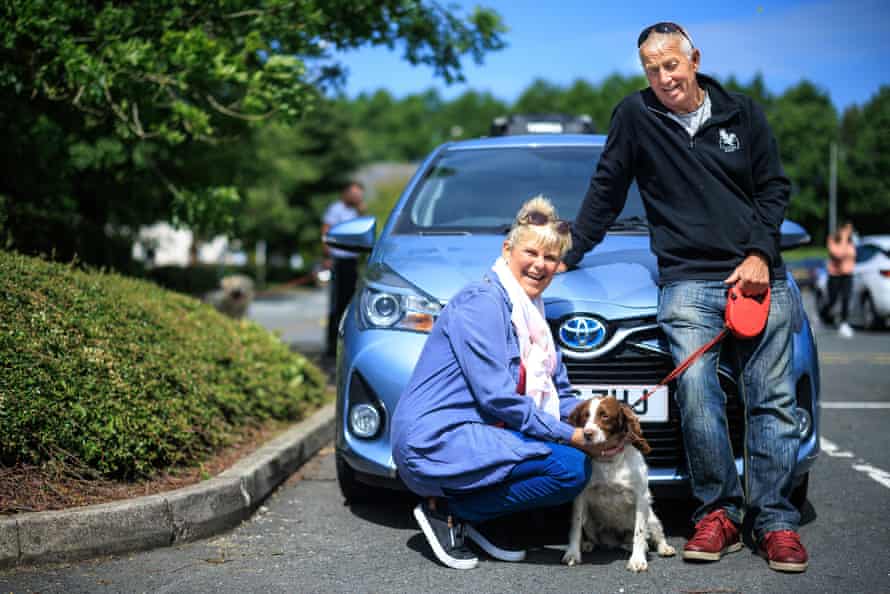 Denise und Steve Walsh mit Hund Lottie neben ihrem blauen Toyota-Hybridauto.