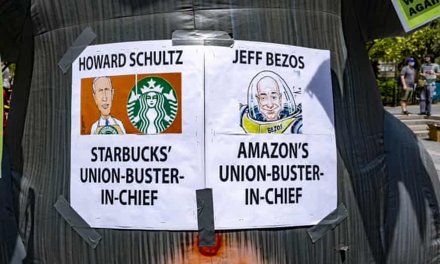 Auf Schildern steht: „Howard Schultz, Starbucks’ Union-Buster-in-Chief“ und „Jeff Bezos, Amazon’s Union-Buster-in-Chief“