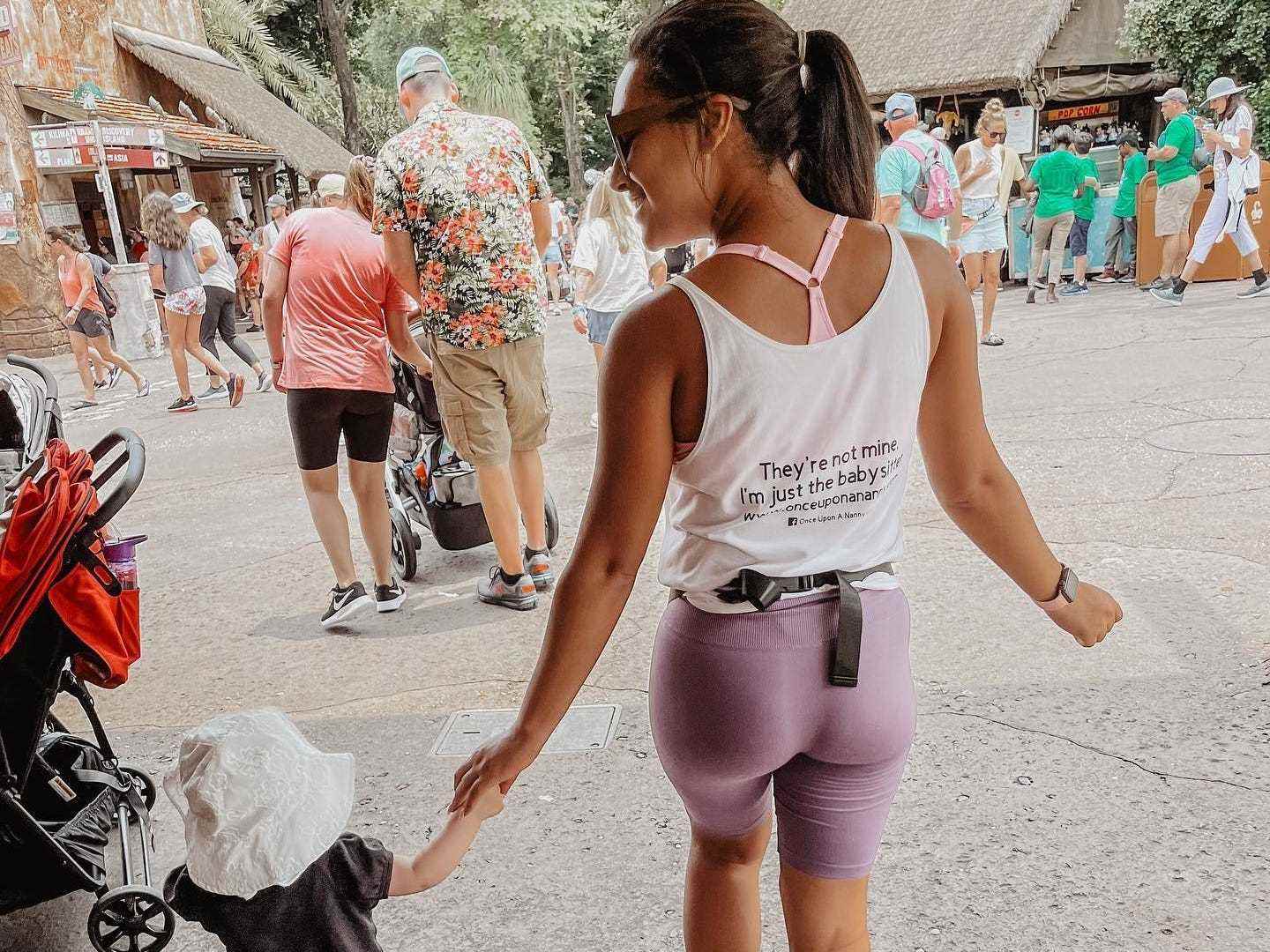 Cyan Nardiello, der dafür bezahlt wird, Kinder in Themenparks zu beaufsichtigen, schlendert Händchen haltend mit einem Kleinkind durch DisneyWorld.  Das Kindermädchen trägt ein T-Shirt mit dem lustigen Satz auf dem Rücken: 