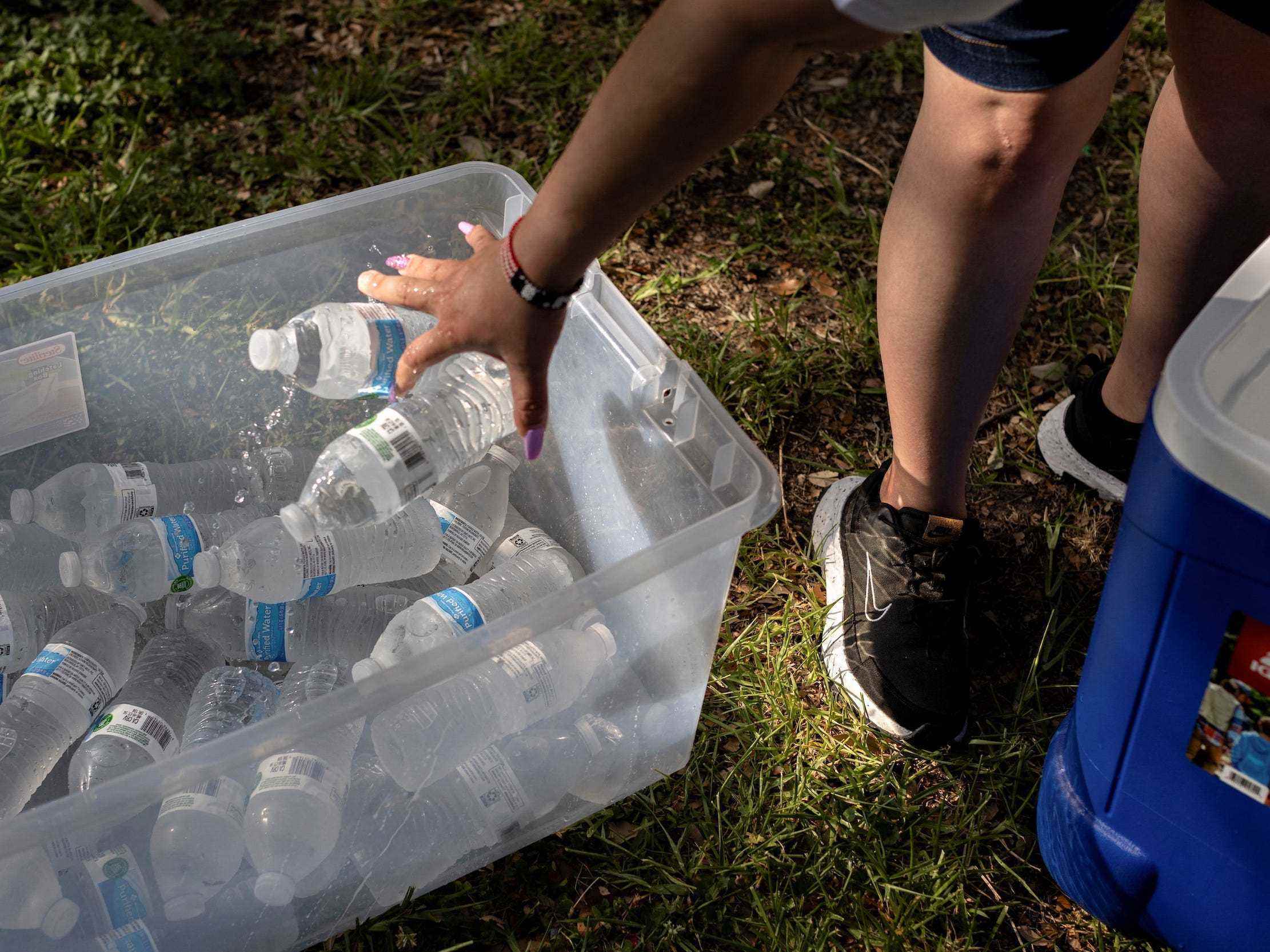 Person wirft Wasserflaschen in einen Plastikeimer