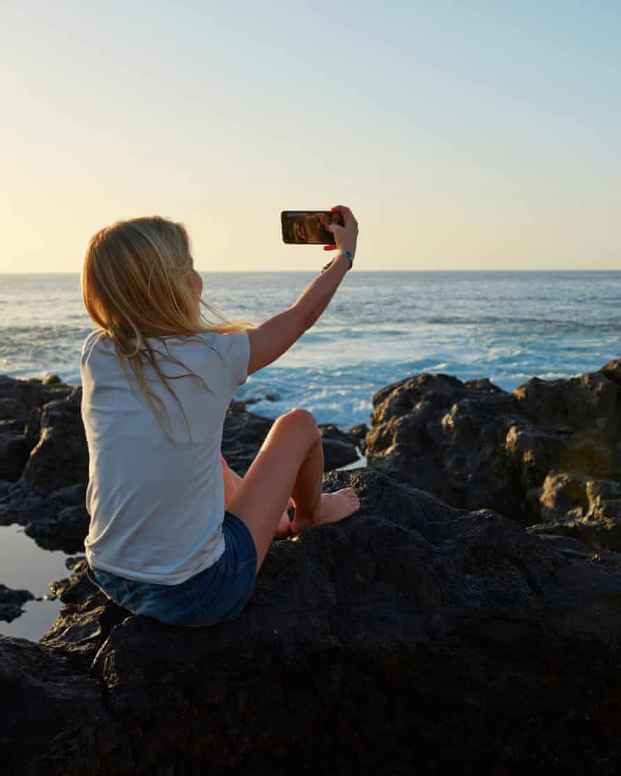 Mädchen, das bei Sonnenuntergang ein Selfie am Meer macht.