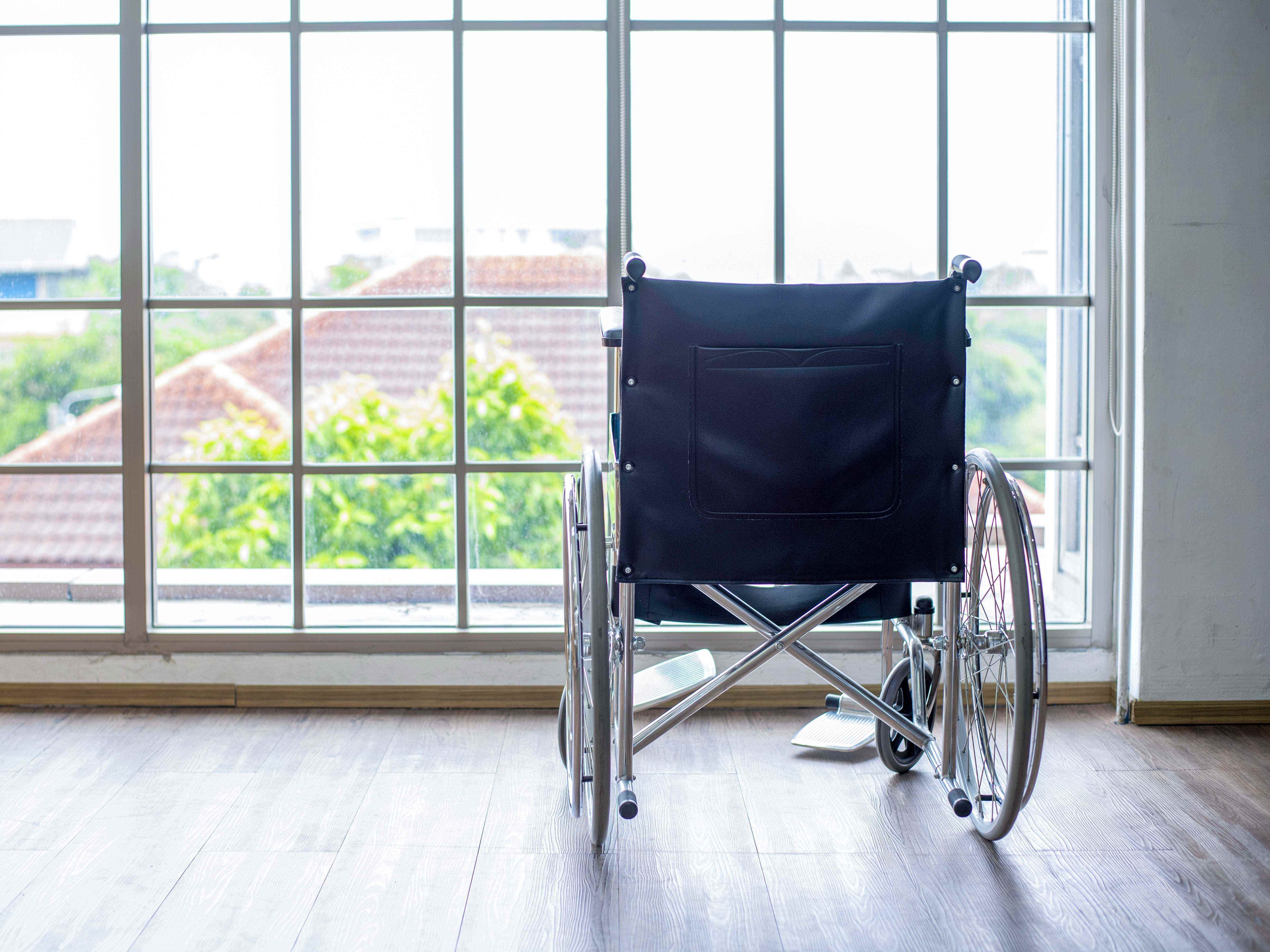 Ein leerer Rollstuhl vor einem großen Glasfenster.