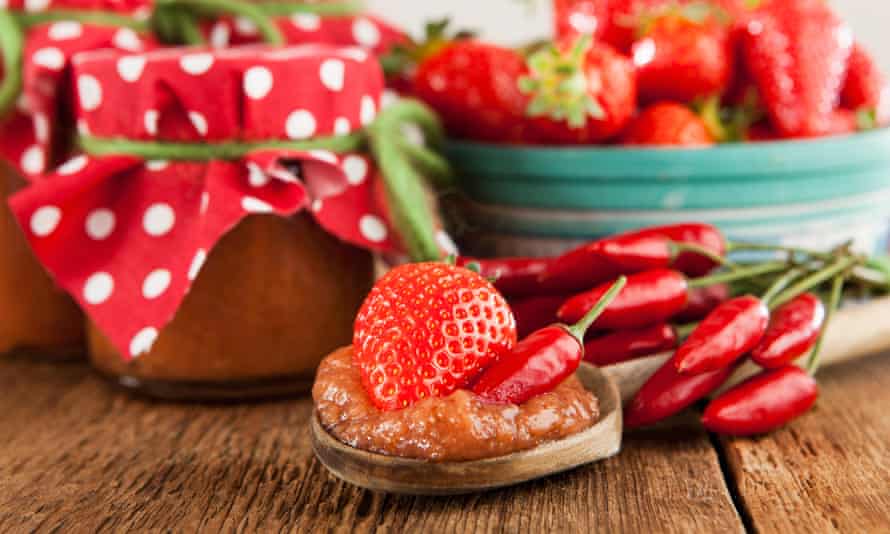 Erdbeer- und Chilimarmelade auf einem Holzlöffel, gekrönt mit einer Erdbeere und einem roten Chili.