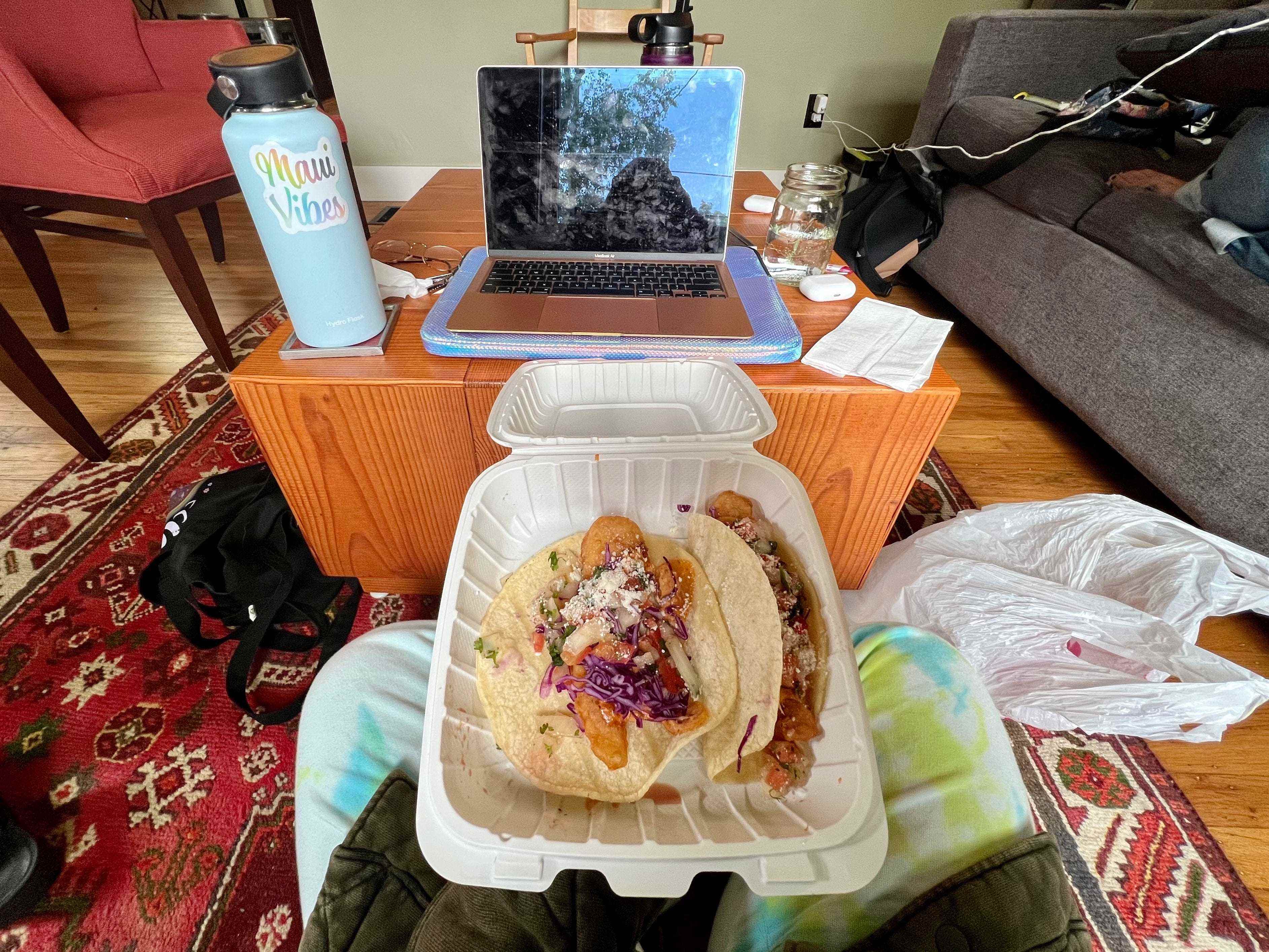 Tacos auf dem Schoß im Container zum Mitnehmen, Laptop im Hintergrund