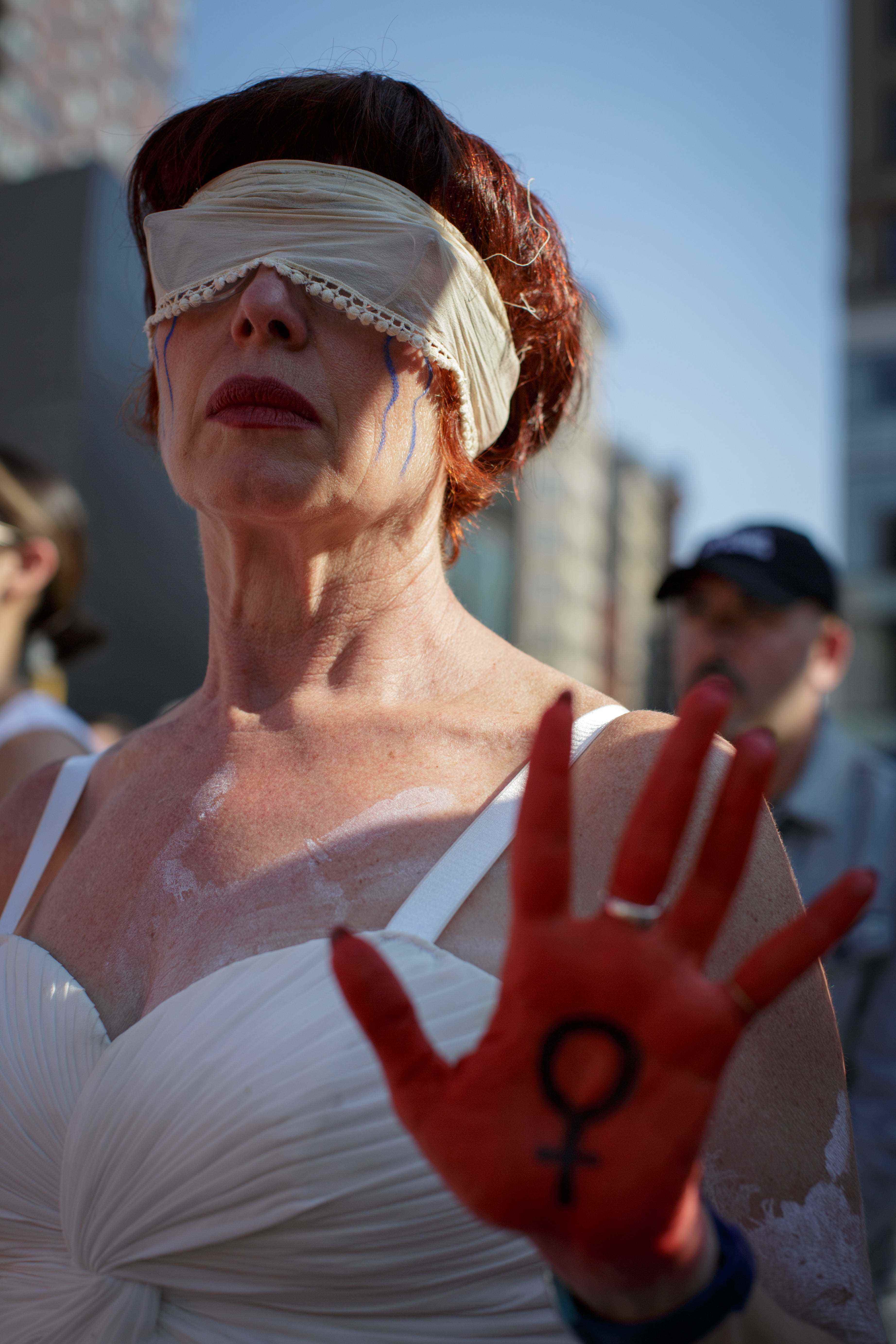 Eine Frau trägt eine Augenbinde und zeigt ihre rot bemalte Hand.