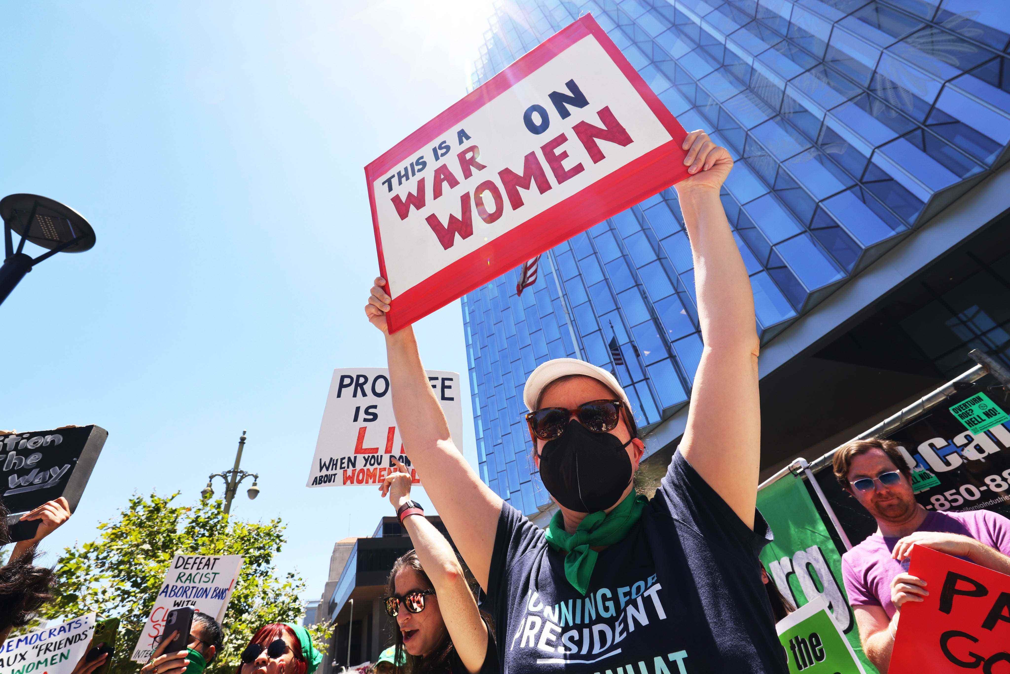 Eine maskierte Person hält ein Schild hoch: „This is a War on Women“.