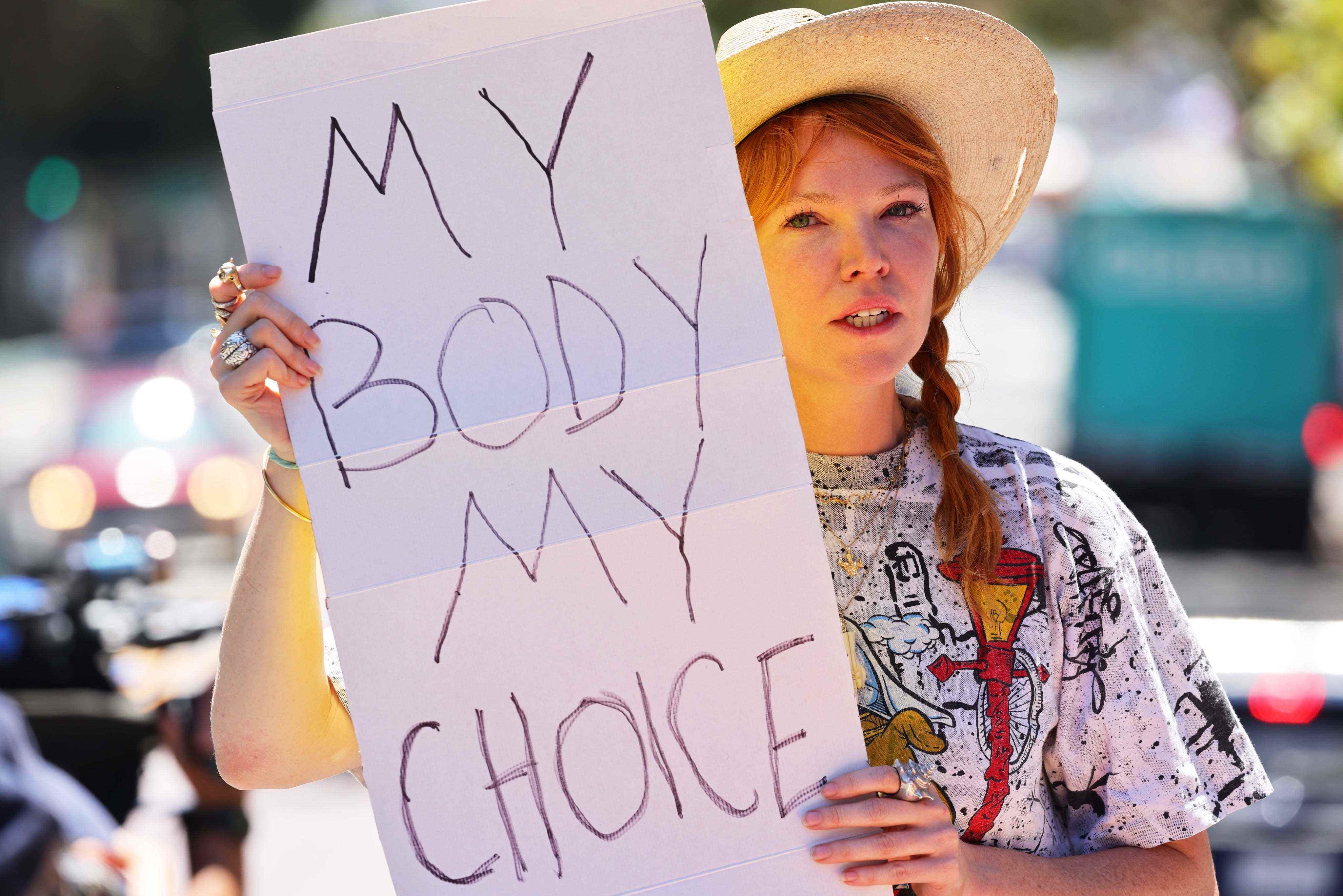 Eine Frau hält ein handgeschriebenes Schild: „Mein Körper, meine Wahl“.