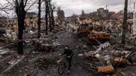 Ein Mann schiebt sein Fahrrad am 6. April 2022 in Bucha, Ukraine, auf einer Straße durch Trümmer und zerstörte russische Militärfahrzeuge.