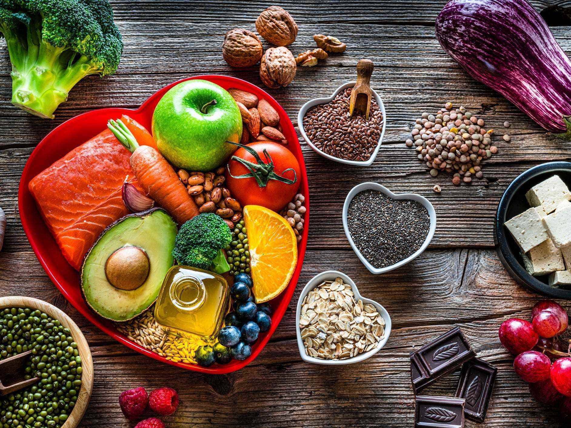 Ein Tisch voller herzgesunder Lebensmittel, darunter Samen, Nüsse, Tofu, grünes Gemüse wie Brokkoli, Avocado, Beeren, Lachs und Obst