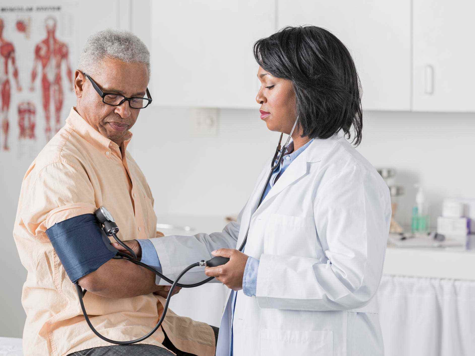 Ein Arzt im weißen Laborkittel führt in einer Arztpraxis einen Blutdrucktest bei einem älteren Patienten mit kurzen grauen Haaren durch