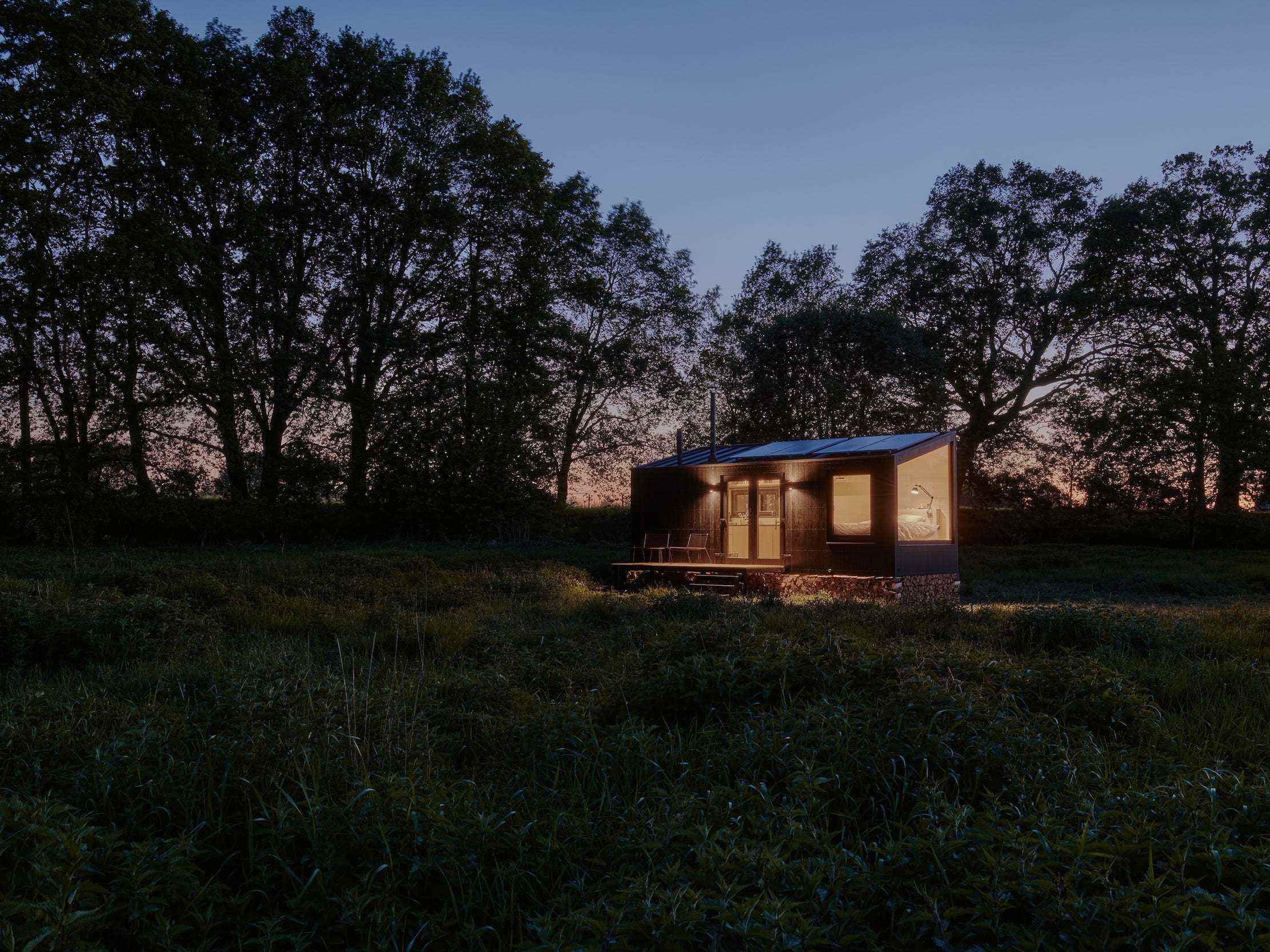 Eine Raus-Hütte in der Natur, umgeben von Bäumen und offenen Feldern bei Nacht.