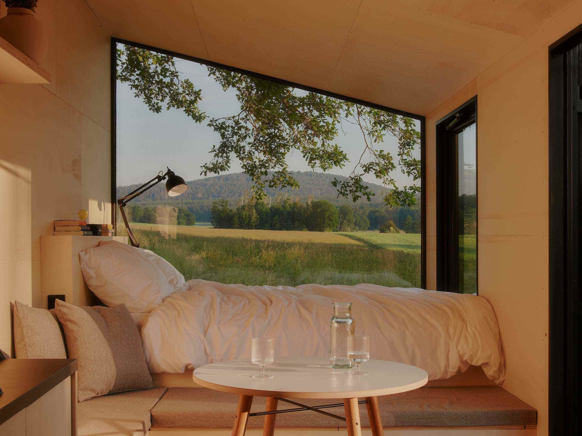 Ein Bett und ein Esstisch neben einem großen Fenster mit Blick in die Natur
