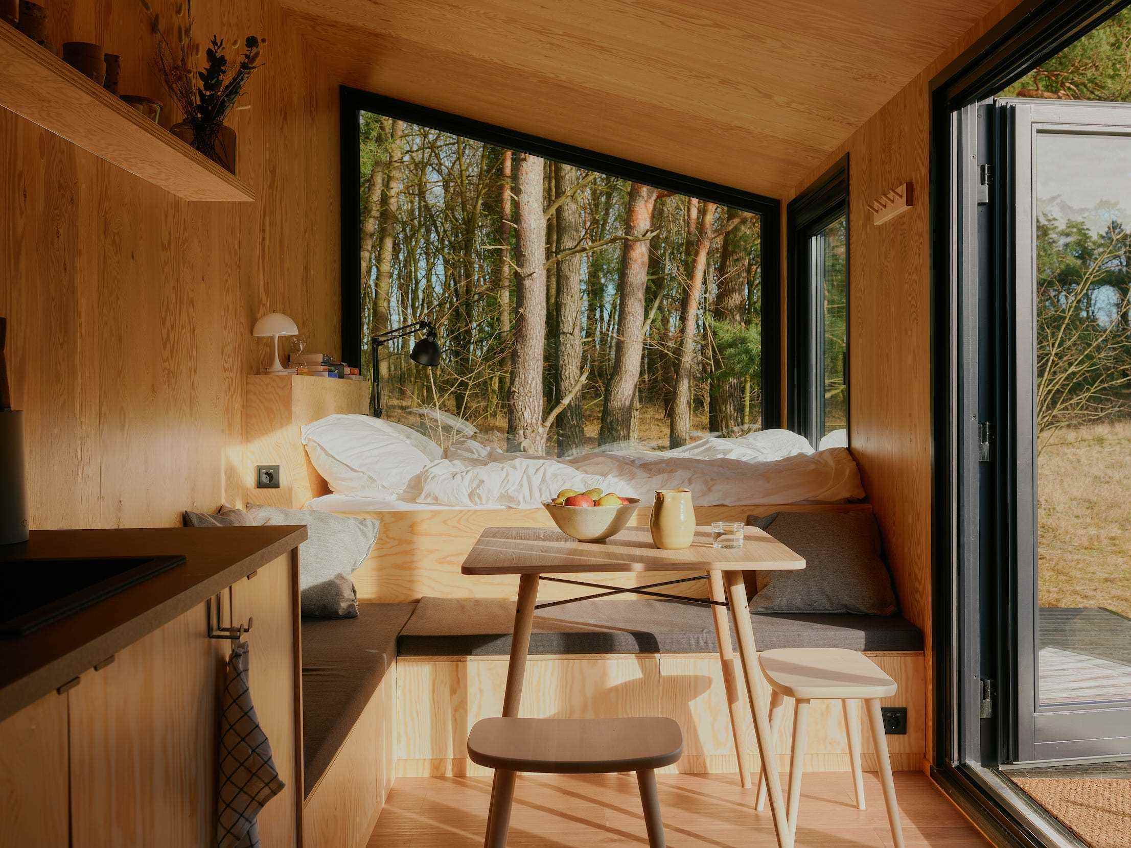 Ein Bett, eine Küche, ein Tisch mit Stühlen und Fenster, die die Natur draußen zeigen