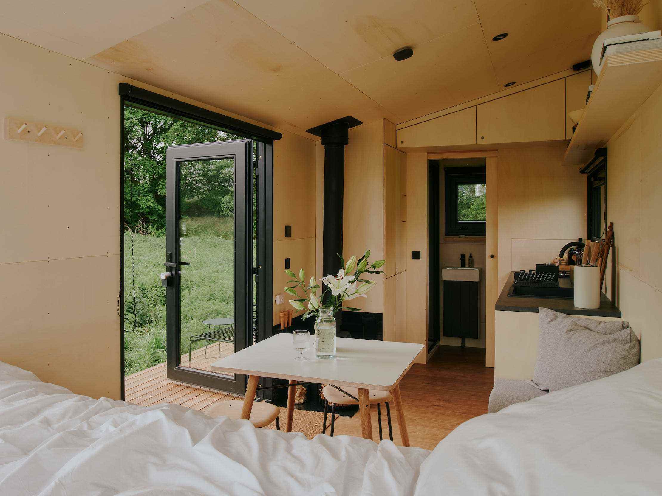 Blick in eine Raus-Hütte mit Bett, Esstisch, Küche, Fenster mit Blick in die Natur.