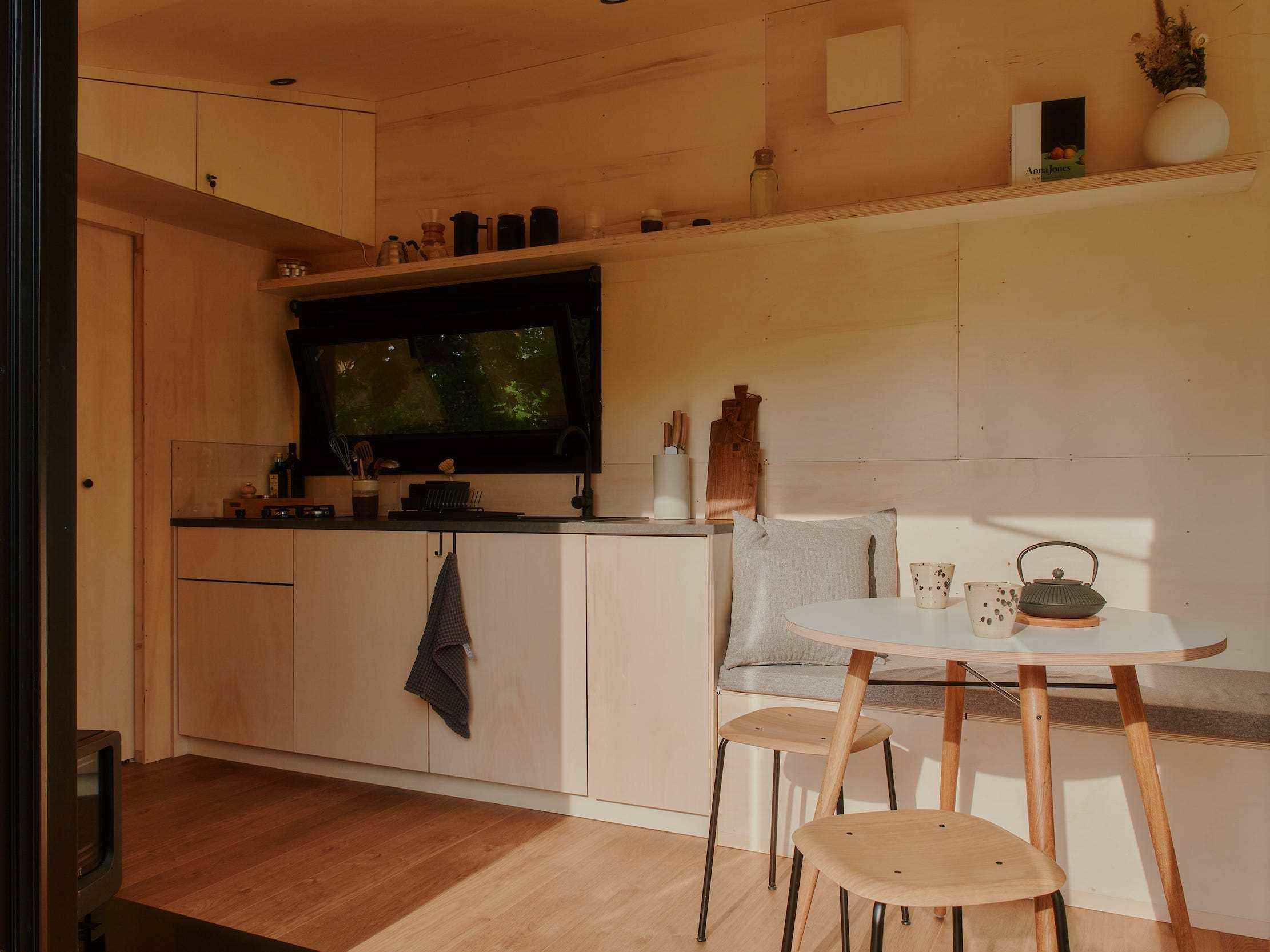 Ein Blick in eine Raus-Hütte mit Esstisch, Küche, Fenstern mit Blick in die Natur.