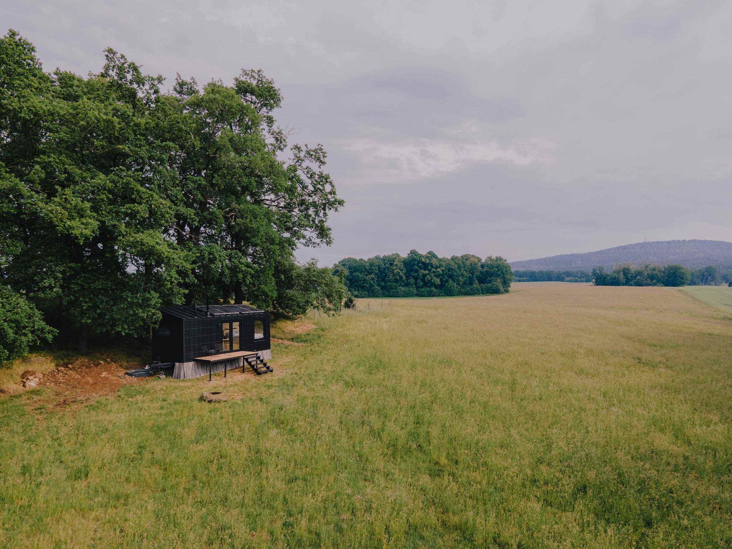 Eine Raus-Hütte draußen in der Natur, umgeben von Bäumen und einem offenen Feld