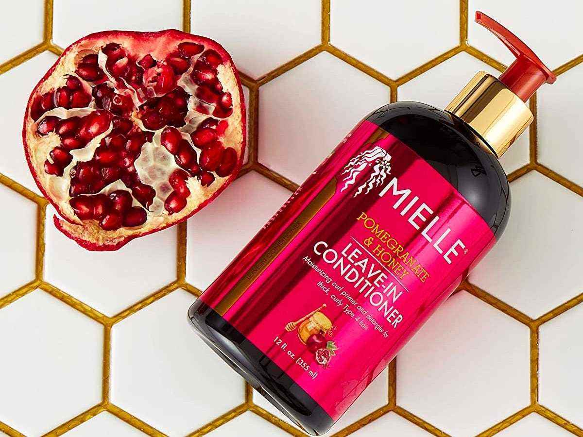 Flasche Mielle Organics Pomegranate & Honey Leave-In Conditioner neben einem Granatapfel auf einer gefliesten Oberfläche