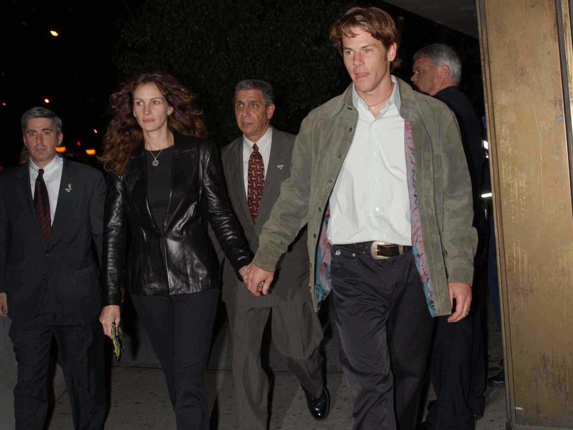 Auf diesem Foto aus dem Jahr 2002 kommt Julia Roberts in einem komplett schwarzen Outfit aus einer Filmvorführung und hält Händchen mit Ehemann Danny Moder, der eine graue Jacke, ein weißes Hemd und eine braune Hose trägt.