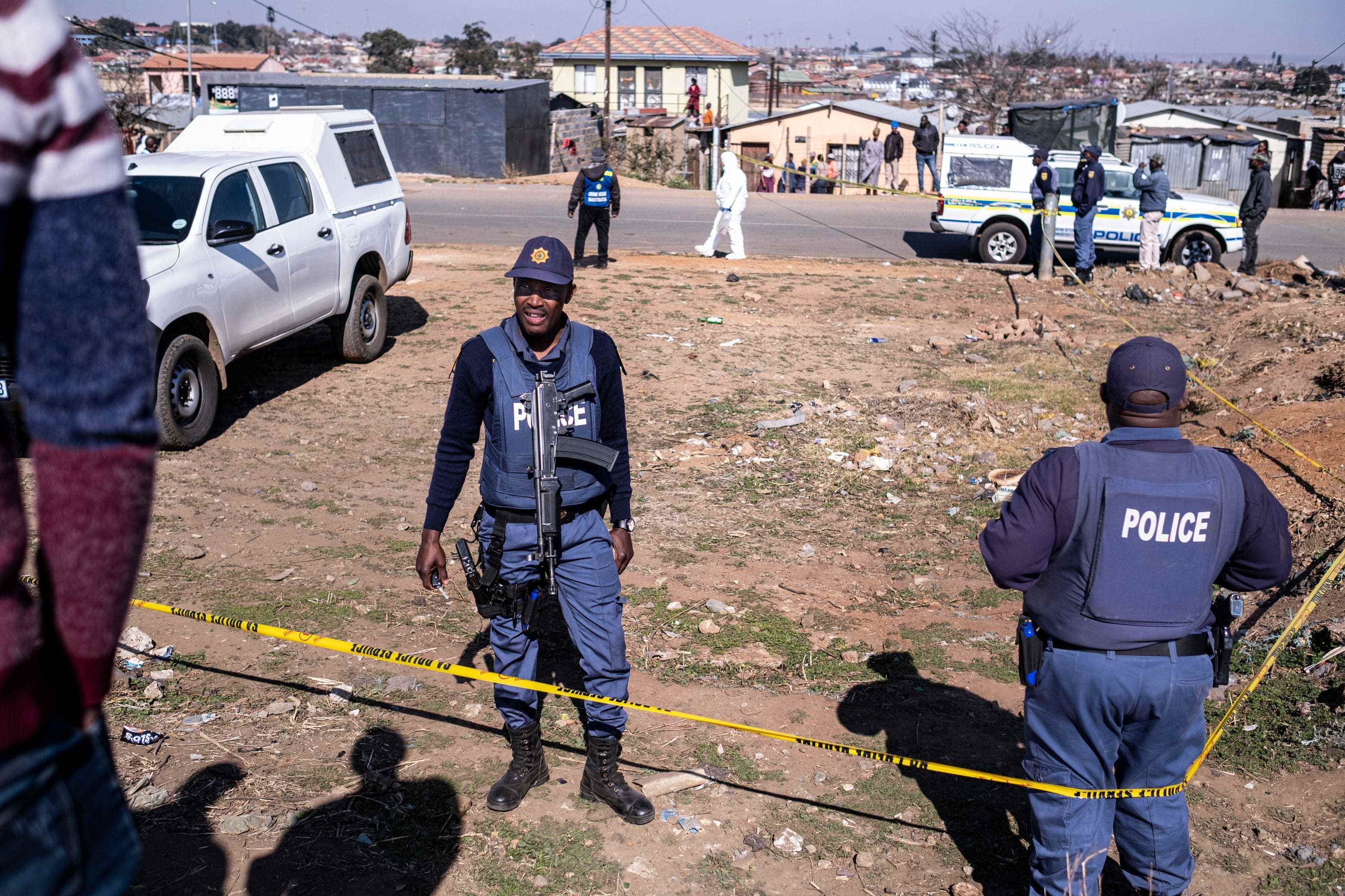 Beamte des südafrikanischen Polizeidienstes (SAPS) erzwingen einen Umkreis um einen Tatort, während Ermittler den Tatort inspizieren, an dem 15 Menschen in einer Taverne erschossen wurden, während ein forensisches Team am 10. Juli 2022 in Soweto ermittelt.