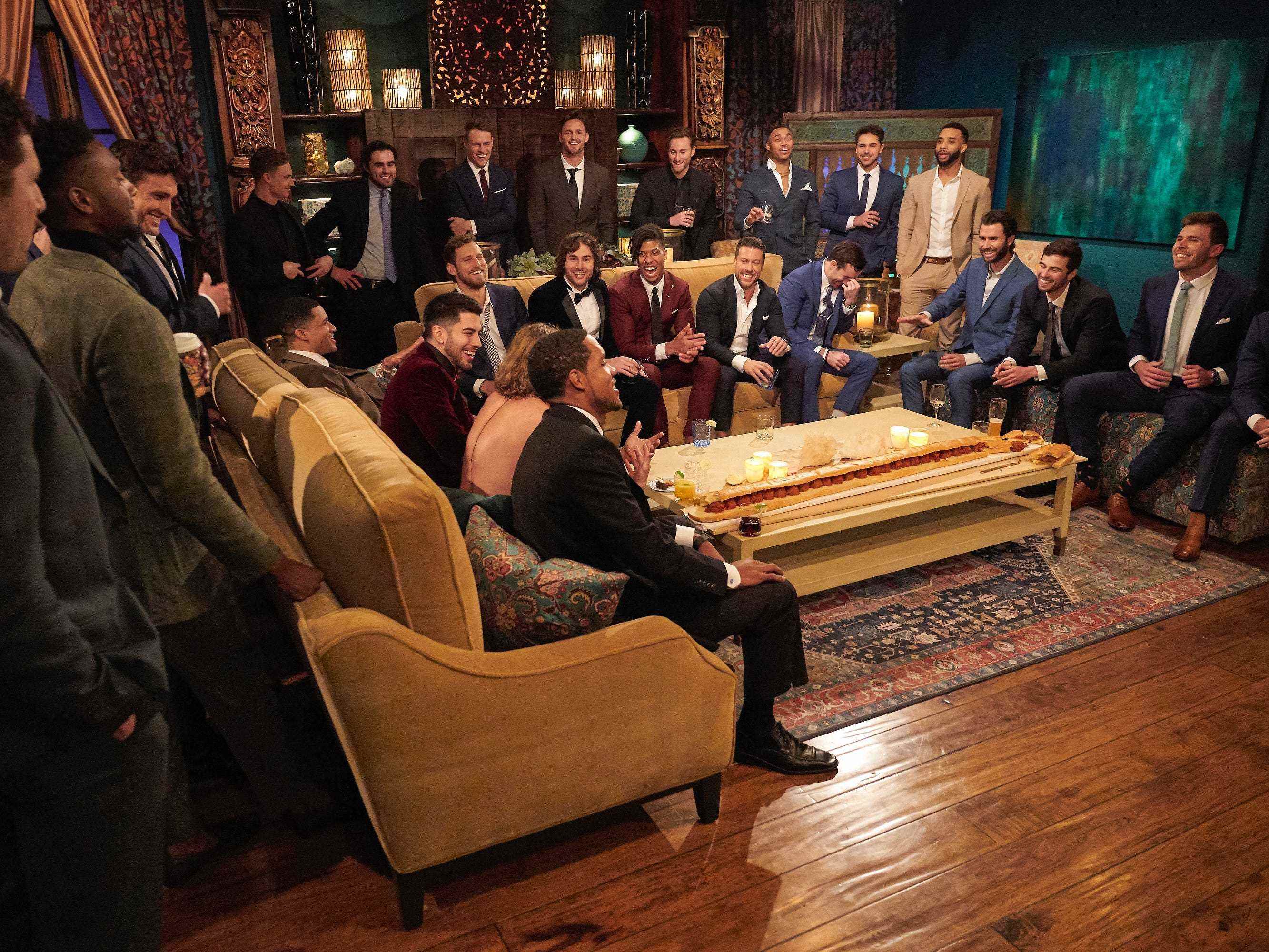 Die männlichen Kandidaten in Anzug und Krawatte versammeln sich in diesem Standbild aus der 19. Staffel von „Die Bachelorette“ um einen Couchtisch.