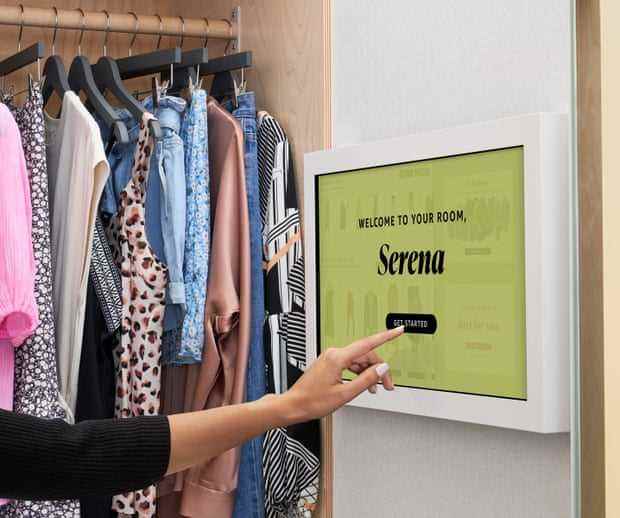Auf einem Touchscreen in einer Umkleidekabine steht „Willkommen in Ihrem Zimmer, Serena“, während sich eine Hand darauf vorbereitet, auf die Schaltfläche „Los geht's“ zu tippen.