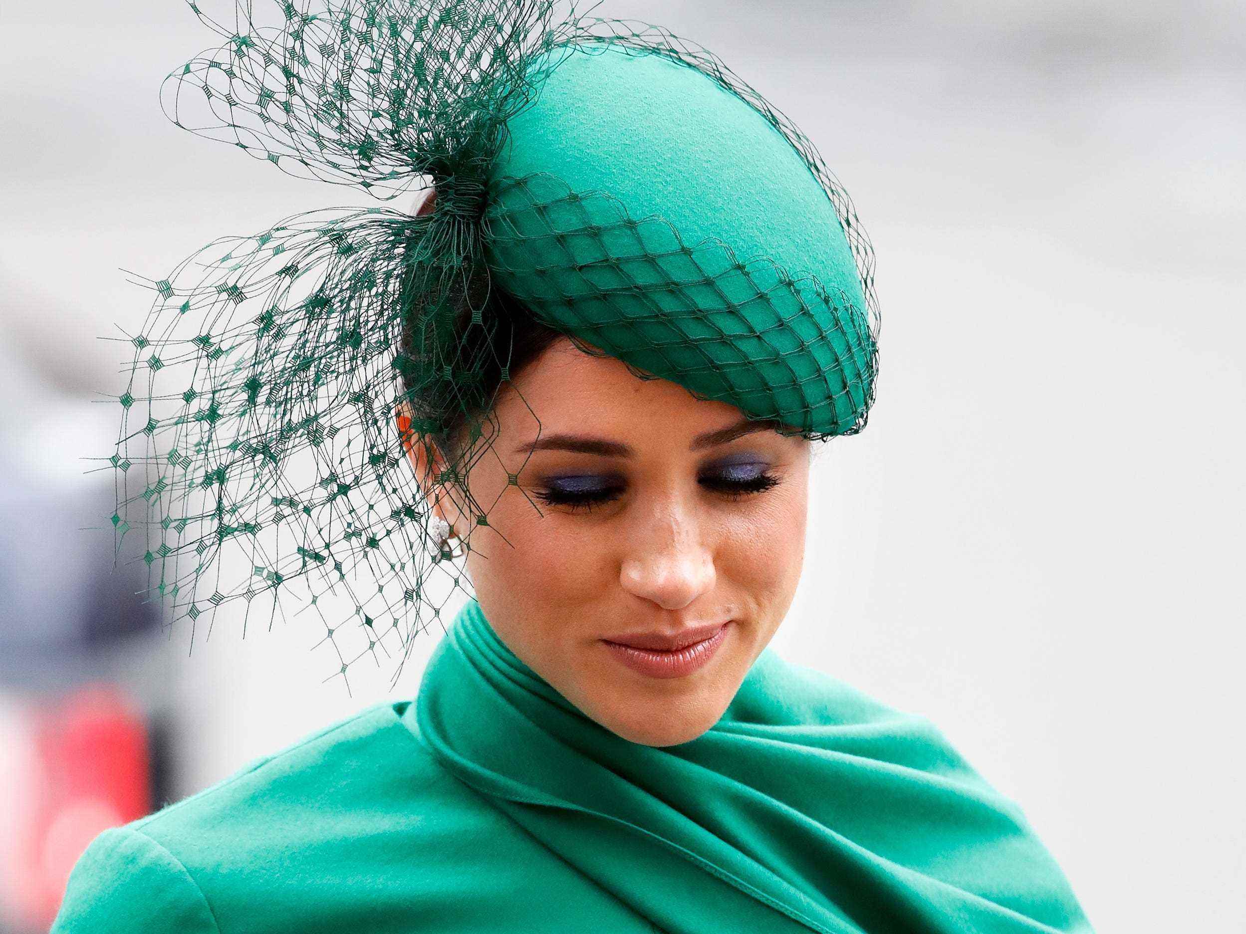 Meghan Markle trägt ein grünes Kleid und einen Hut und blickt nach unten