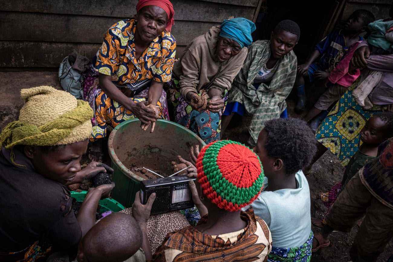 Mitglieder der Gemeinde im Dorf Chibuga hören Radio, während sie Tonkugeln rollen und sie mit Holzkohle überziehen, um sie als Brennstoff zu verkaufen