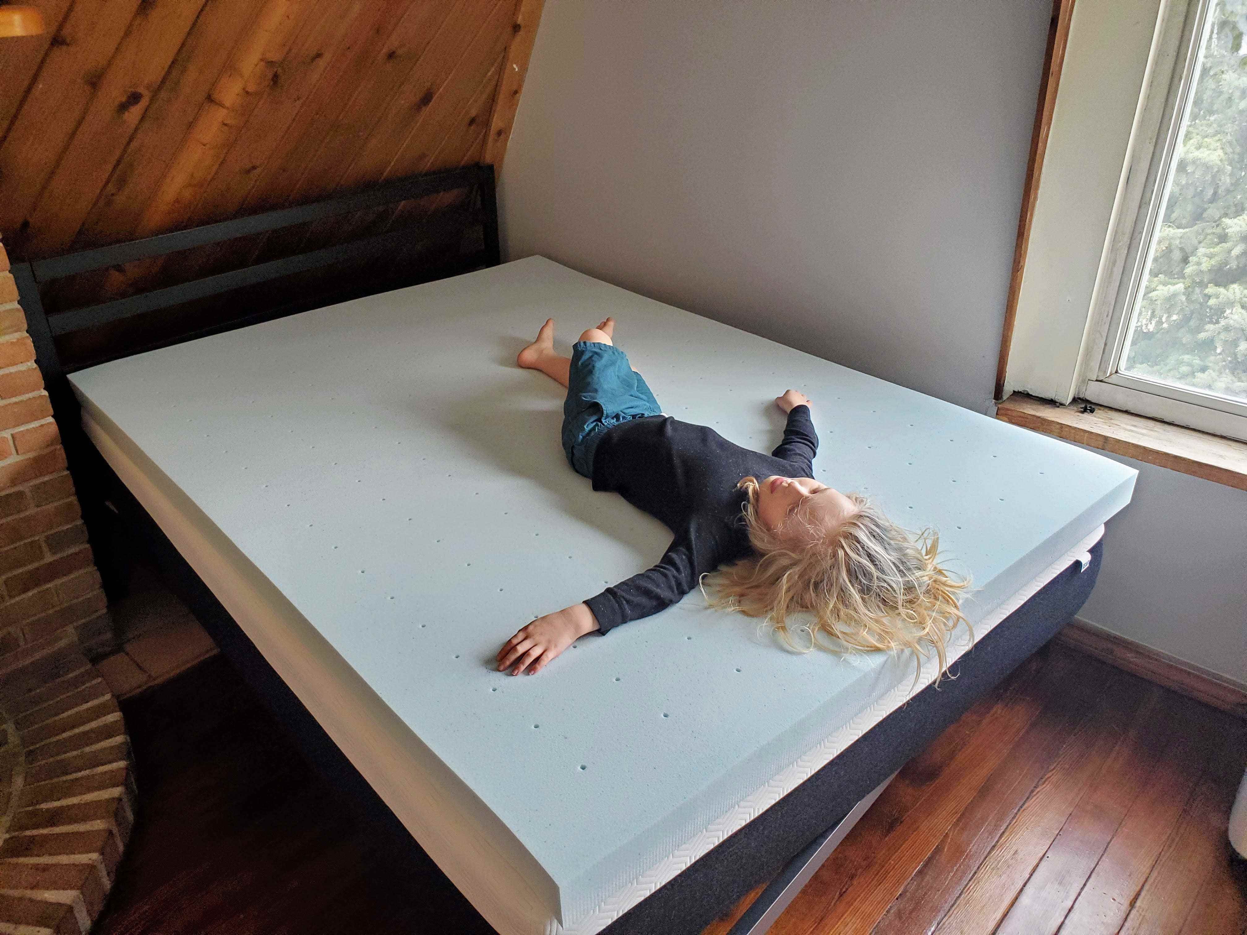 Ein kleiner Junge, der auf einer Schaumstoff-Matratzenauflage auf einem Bett liegt, beste Matratzenauflagen 2022