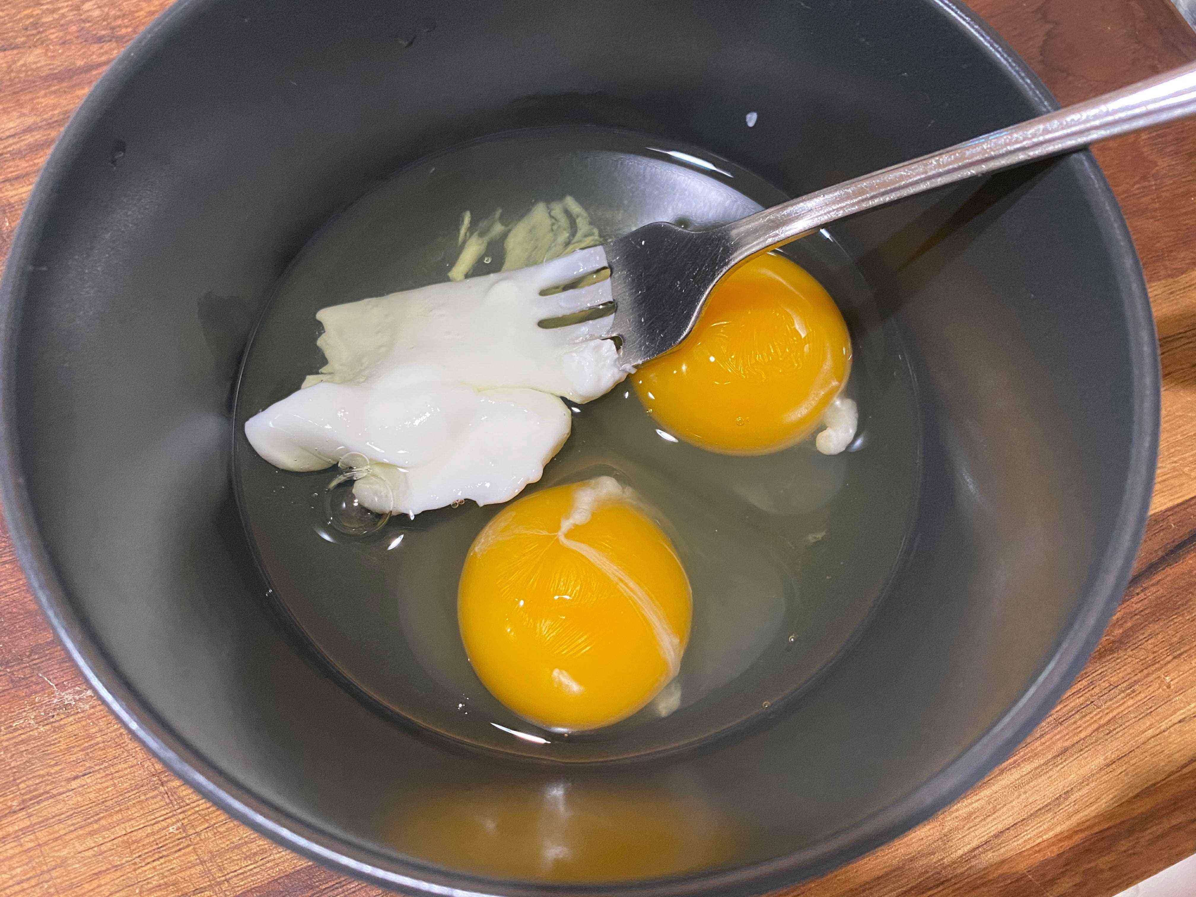 ein Löffel griechischer Joghurt in einer Schüssel mit zwei aufgeschlagenen Eiern