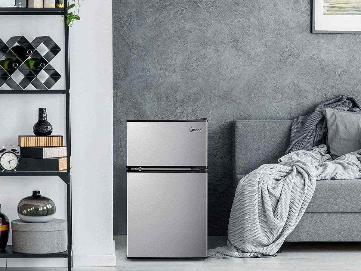 Der Midea Mini-Kühlschrank steht neben einem Sofa und einem Regalsystem.