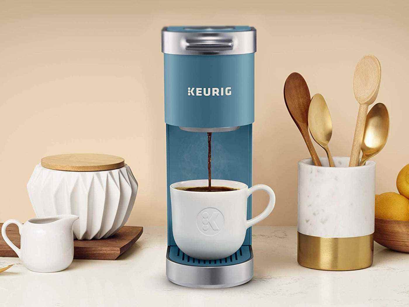 Die Keurig K-Mini Single Serve Kaffeemaschine in Blau gießt Kaffee in eine Tasse und steht neben einem Utensilienhalter.