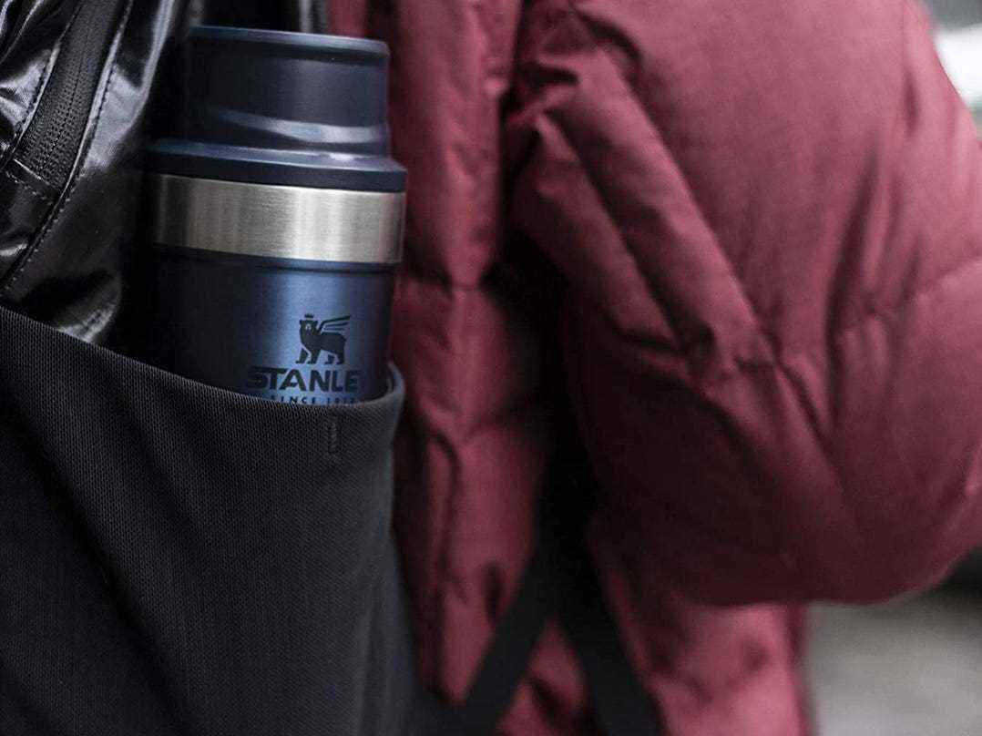 Eine Person trägt den Stanley Classic Trigger Action Travel Mug in ihrem Rucksack.