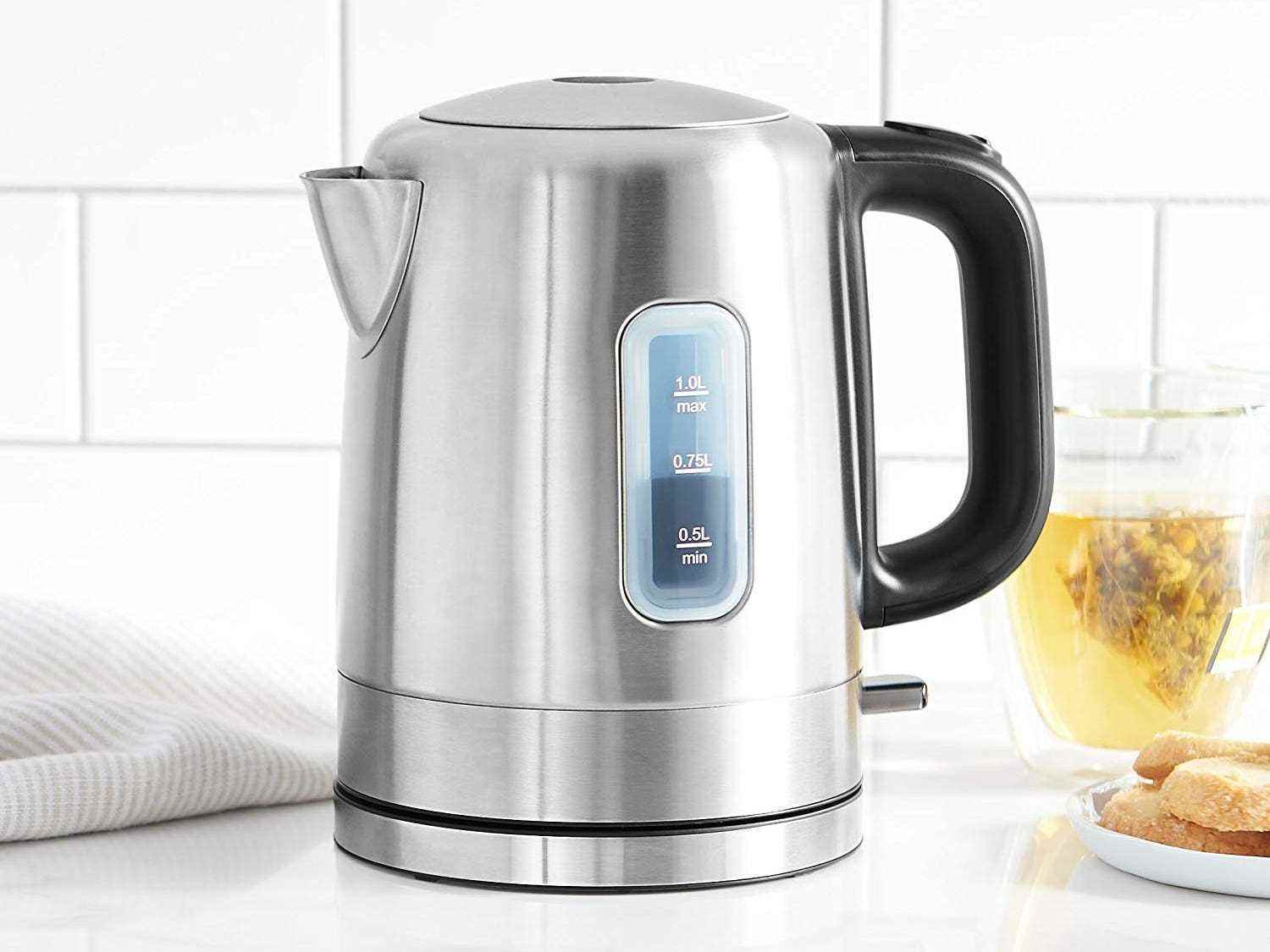 Der Edelstahl-Wasserkocher von AmazonBasics steht auf einer weißen Küchentheke mit einer Teetasse dahinter.