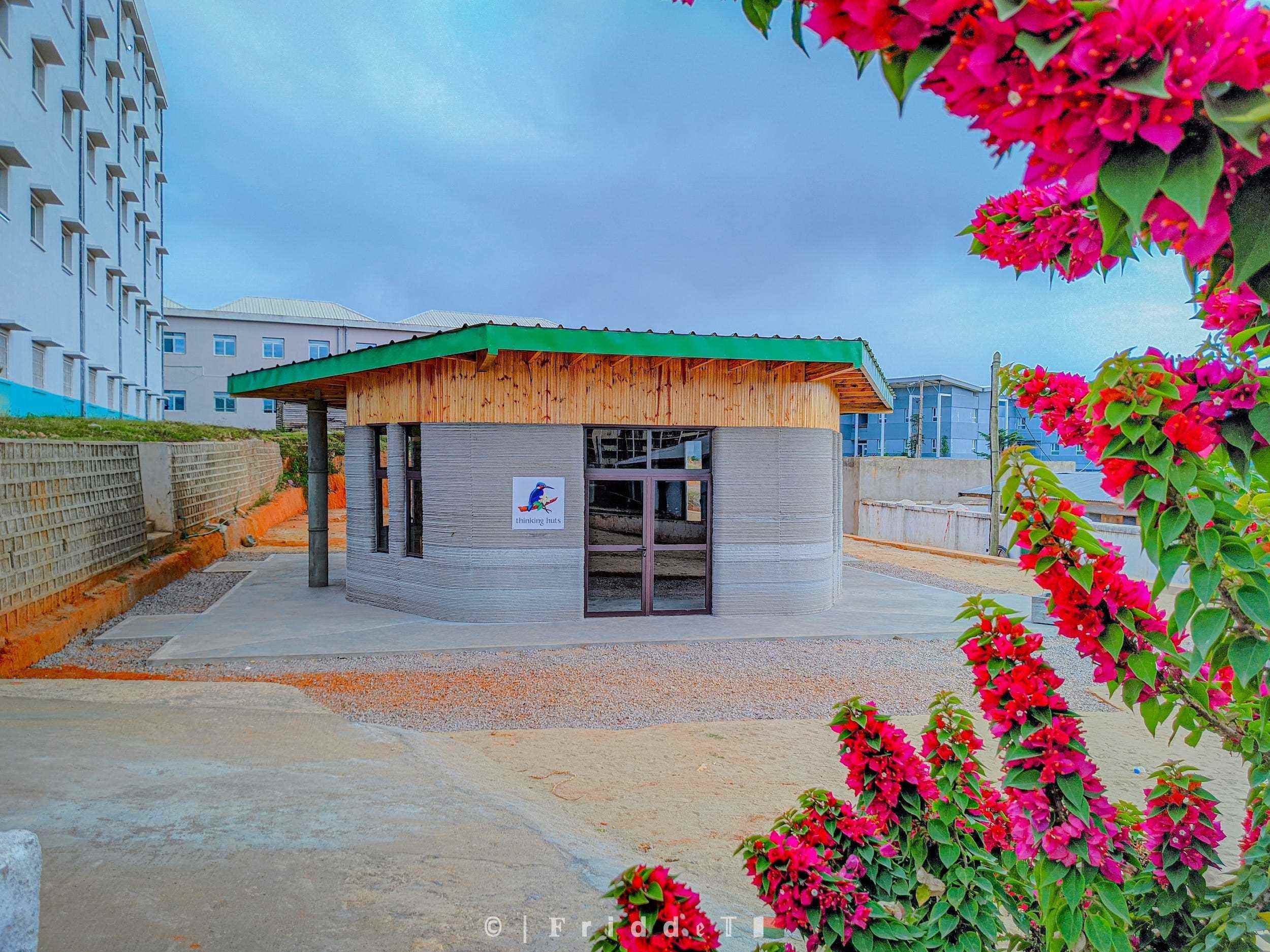 Das 3D-gedruckte Schulgebäude von Thinking Huts mit Blumen im Vordergrund.