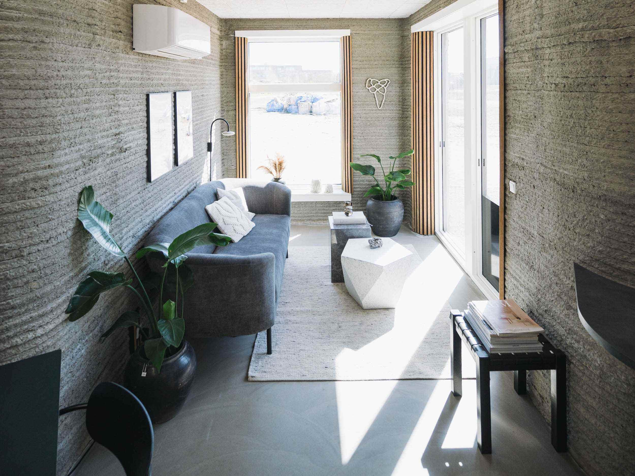 Im Inneren des 3D-gedruckten winzigen Hauses der 3DCP Group mit einem Wohnzimmer, das mit einer Couch, Kunst und großen Fenstern ausgekleidet ist.