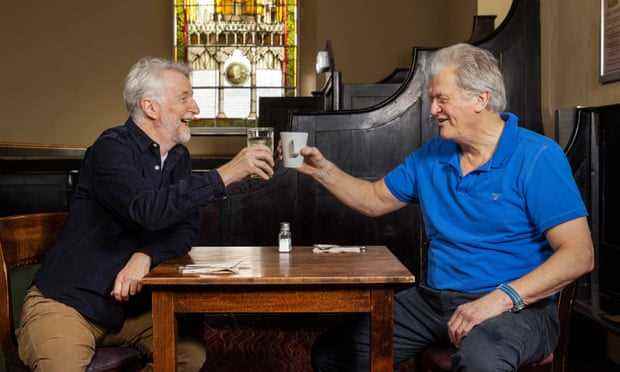 Billy Bragg und Tim Martin stoßen mit ihren Getränken an einem Tisch im George's Meeting House Pub in Exeter an