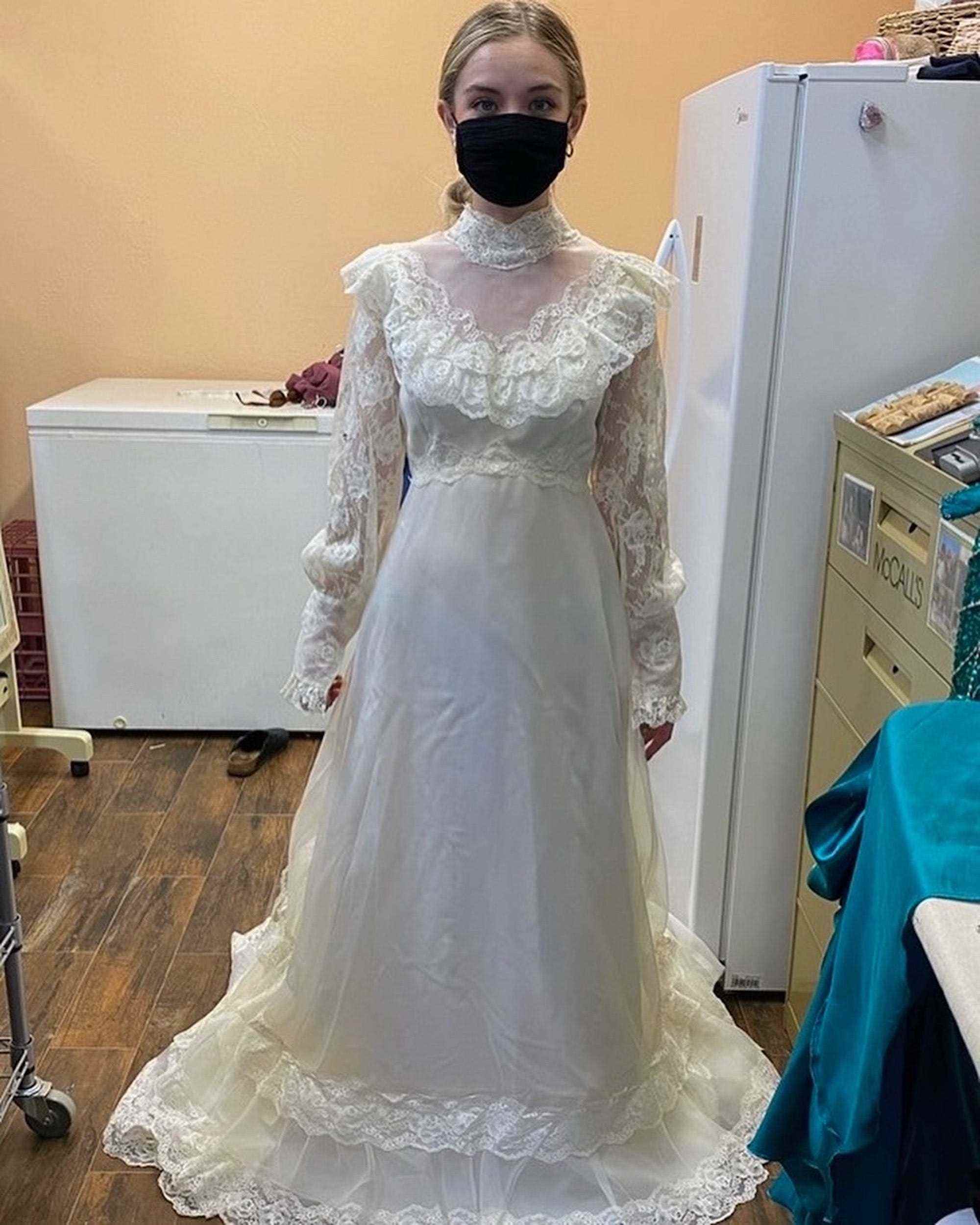 Eine Braut steht in einem langärmligen Hochzeitskleid in einer Näherei.