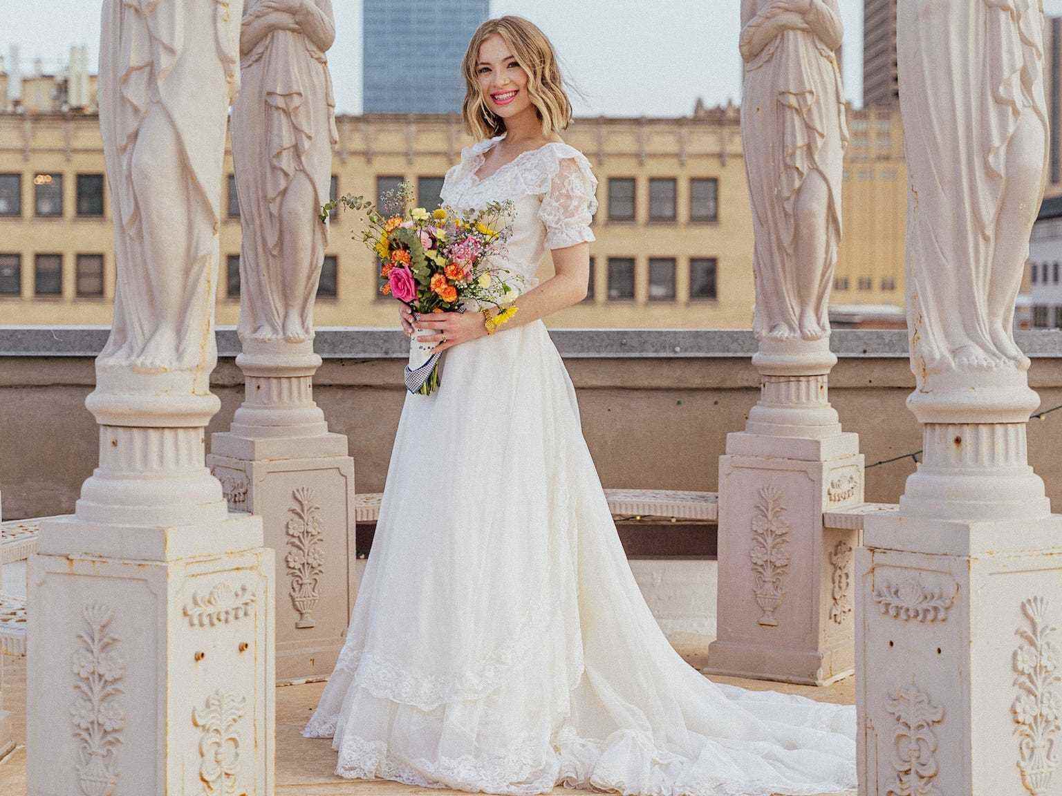 Eine Braut steht in ihrem Hochzeitskleid inmitten von Statuen.