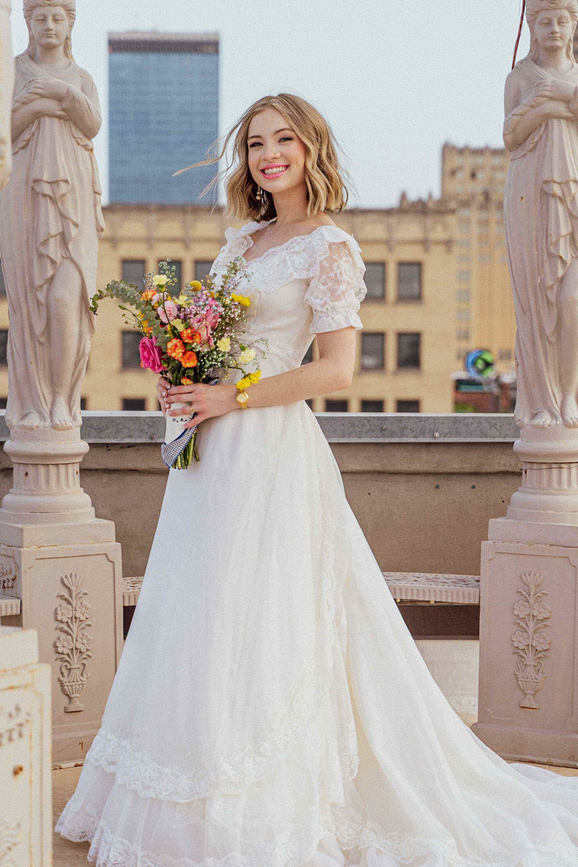 Eine Braut lächelt in ihrem Hochzeitskleid inmitten von Statuen.
