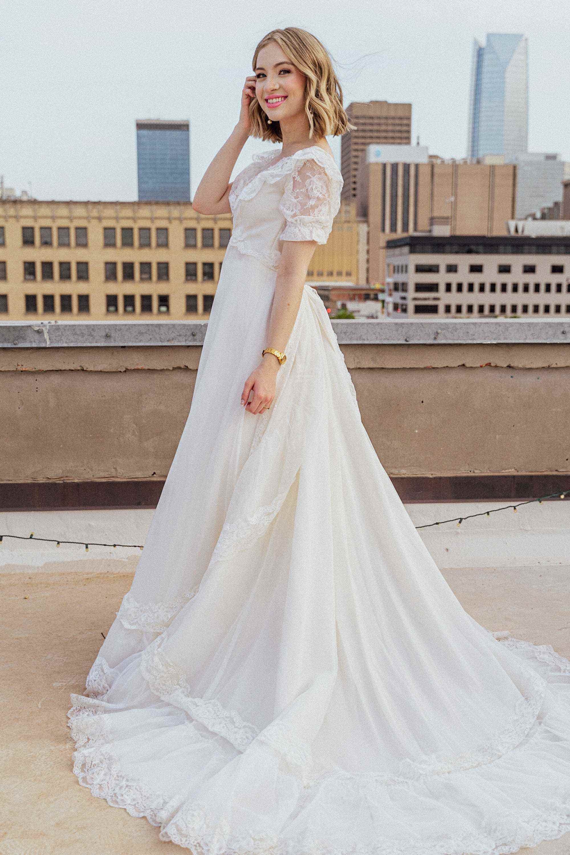 Eine Braut lächelt in ihrem Hochzeitskleid auf einem Dach.