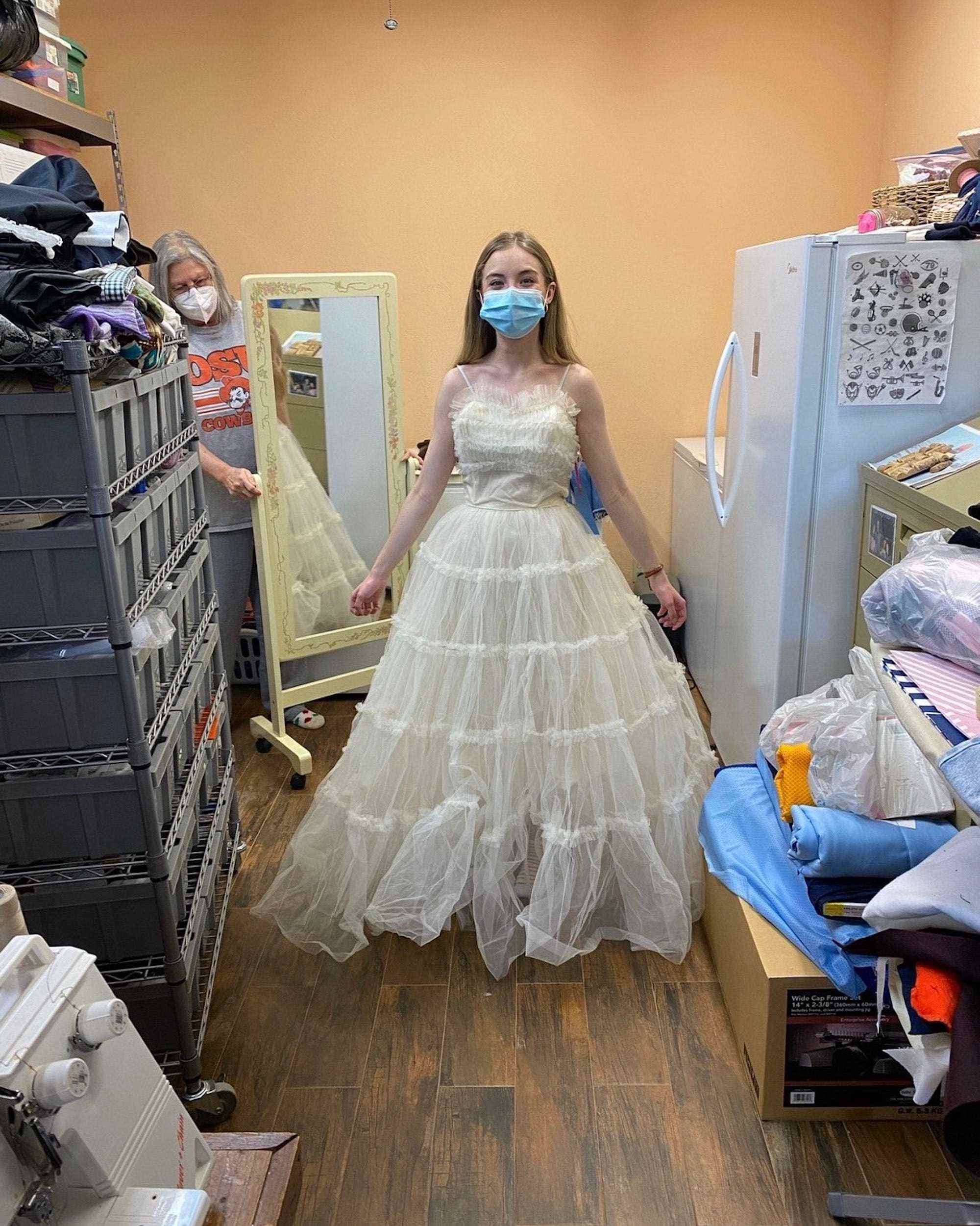 Eine Braut steht in einem schulterfreien Hochzeitskleid in einem Schneidergeschäft.
