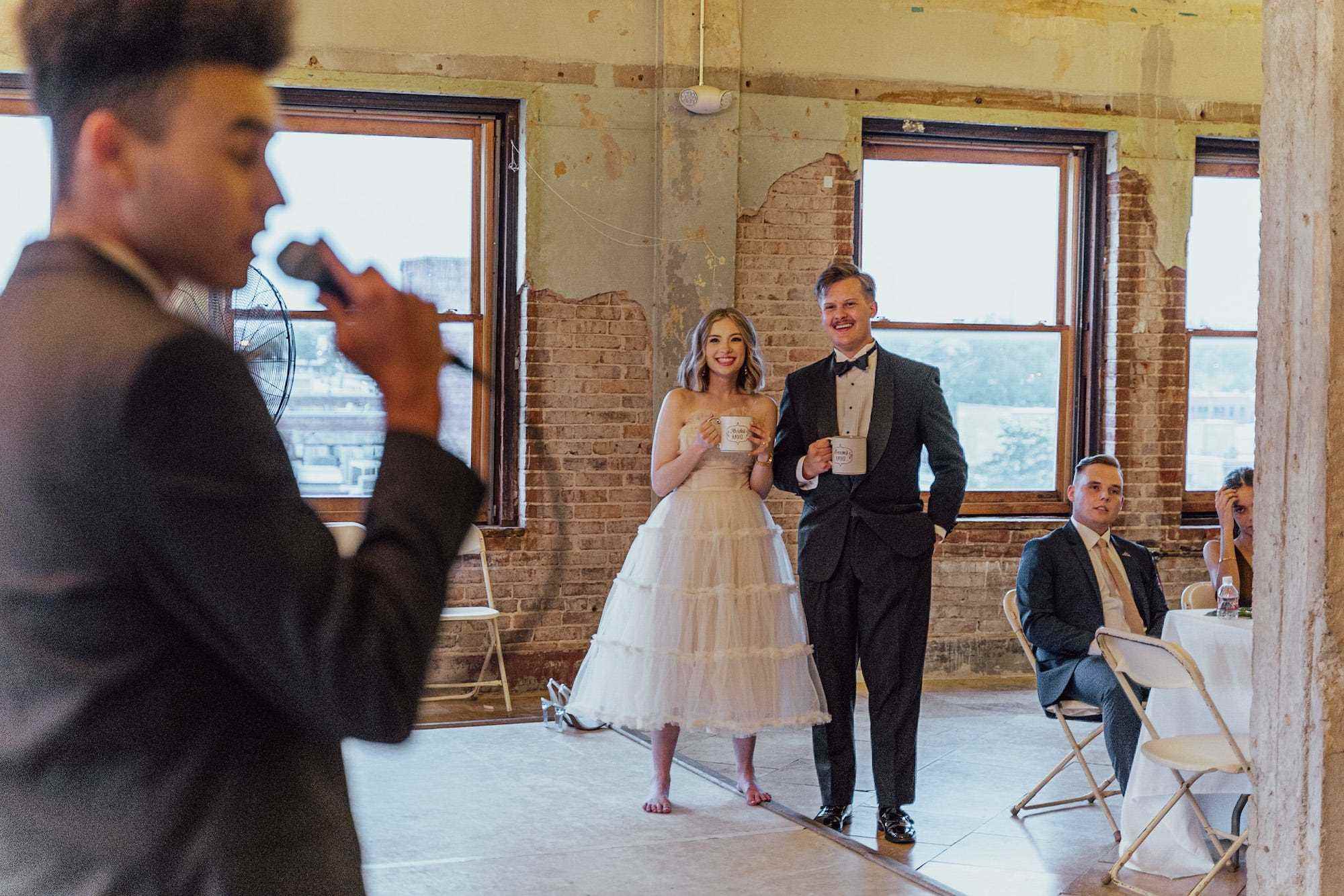 Eine Braut und ein Bräutigam sehen zu, wie jemand bei ihrem Hochzeitsempfang anstößt.