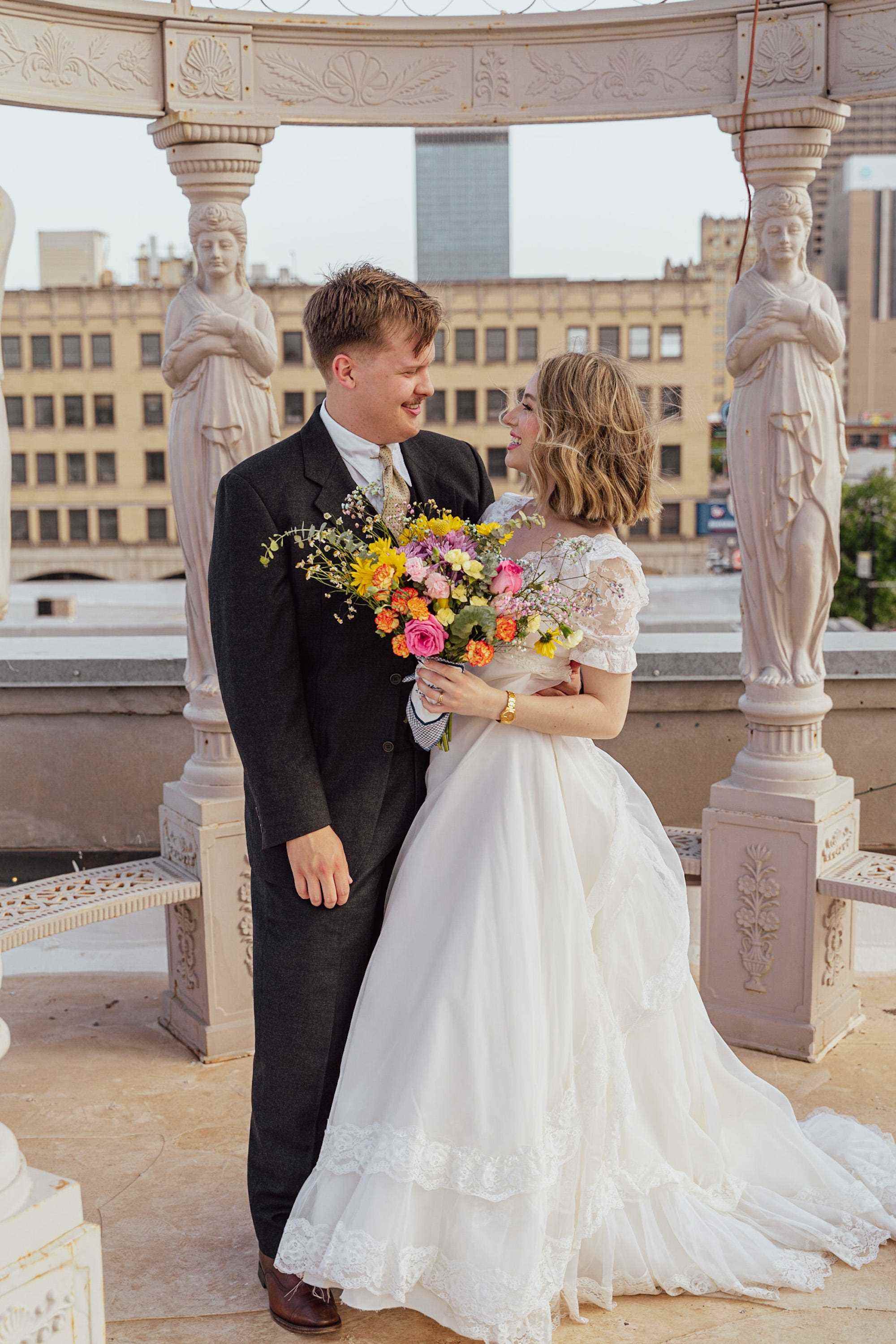 Eine Braut und ein Bräutigam sehen sich in ihrer Hochzeitskleidung vor Statuen an.
