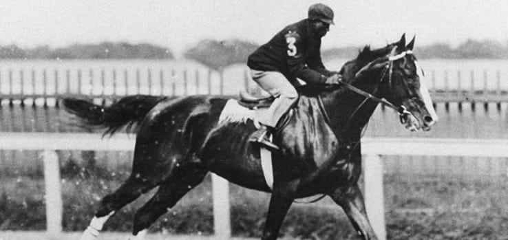 Schwarzer Jockey James Winkfield, der auf einem Pferd läuft.